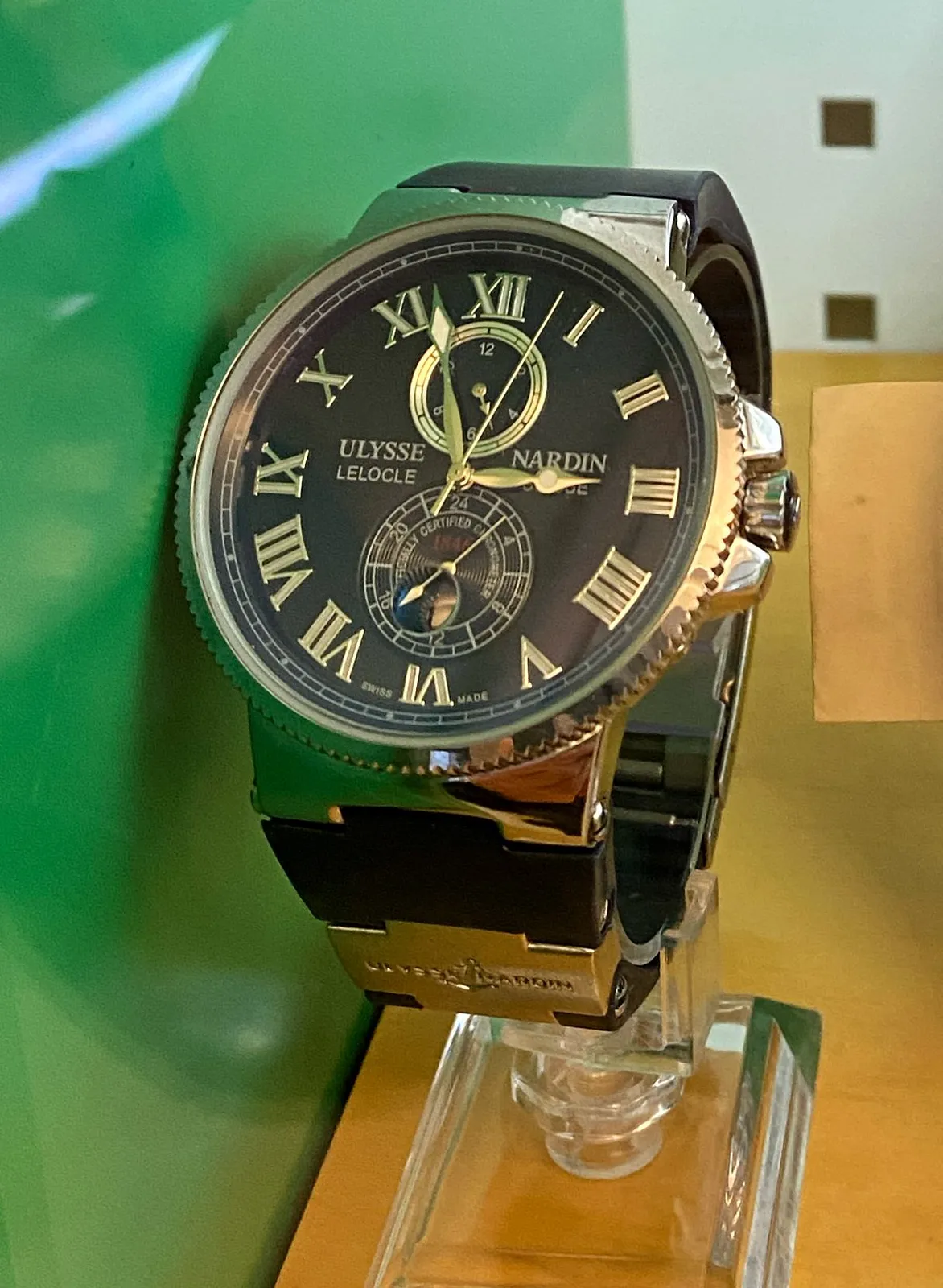 A large shiny Ulysse Nardin wrist watch. Black and gold. It points at 4 minutes to 3. 