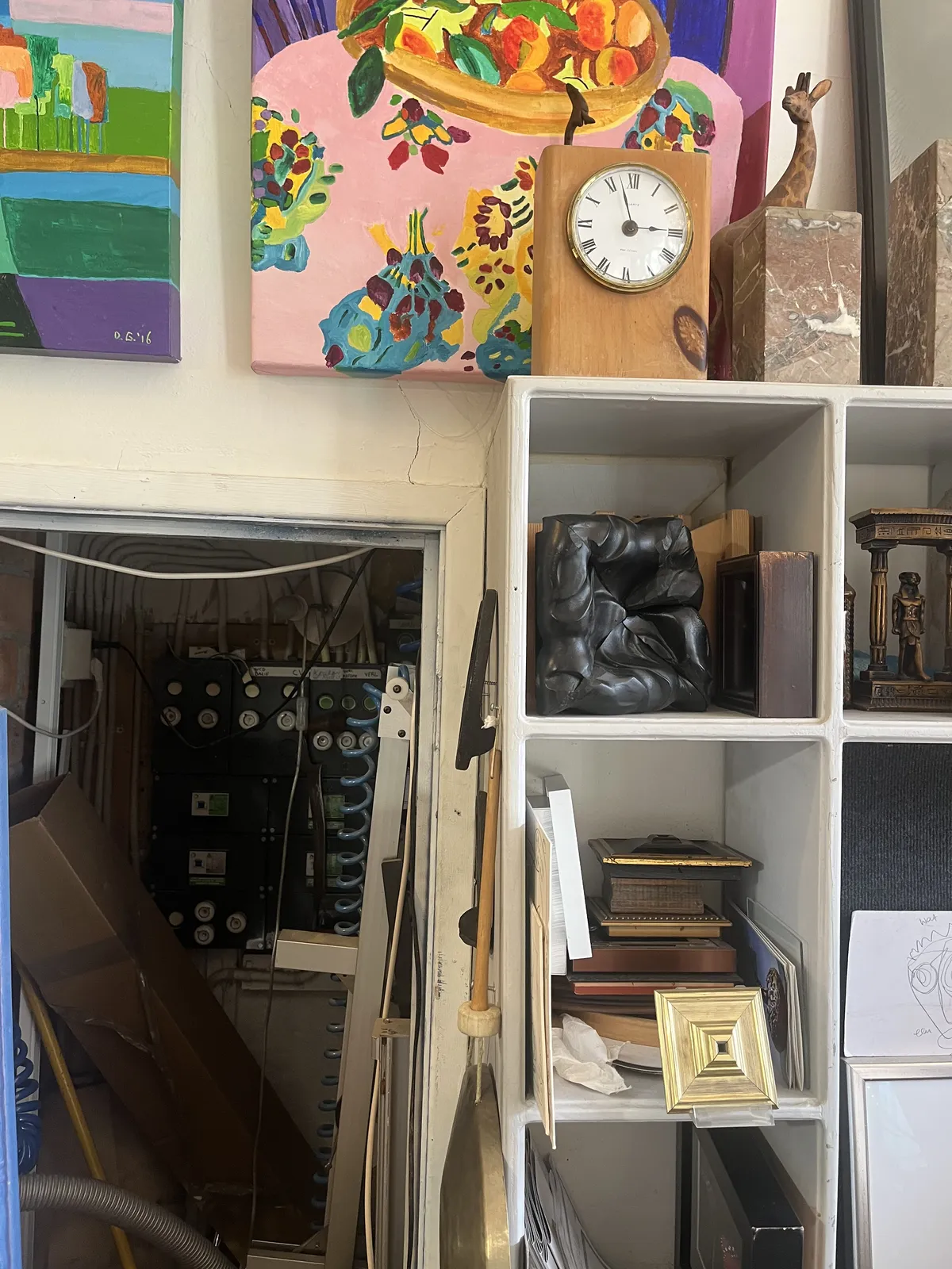 Lots of works of art on the wall and in a cupboard. And a peek into the meter cupboard. There’s also a simple small, wooden clock standing on the cupboard, next to a giraffe. It points at three minutes to three.