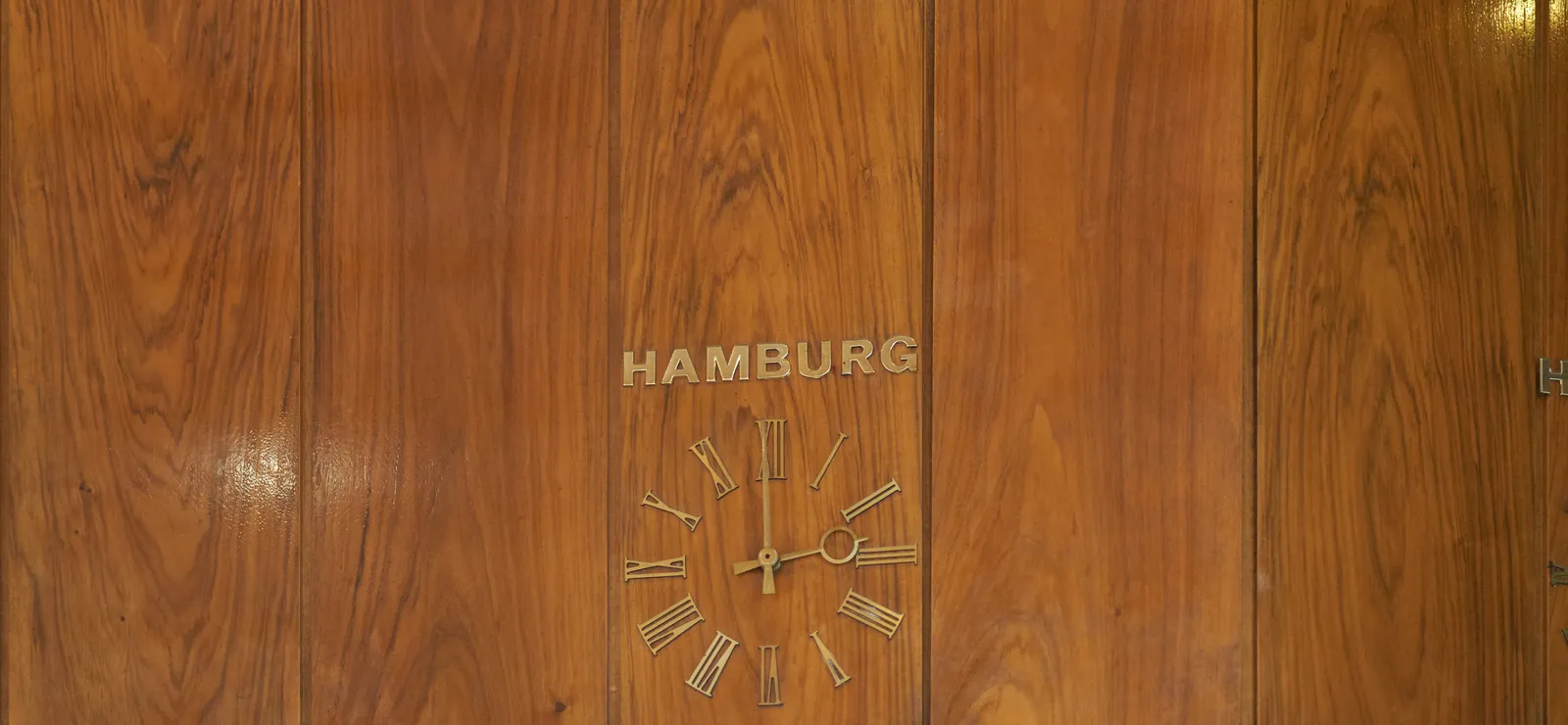 A lathed wall with a built in clock. Above the clock it says Hamburg. The clock points at 1 minute to three.