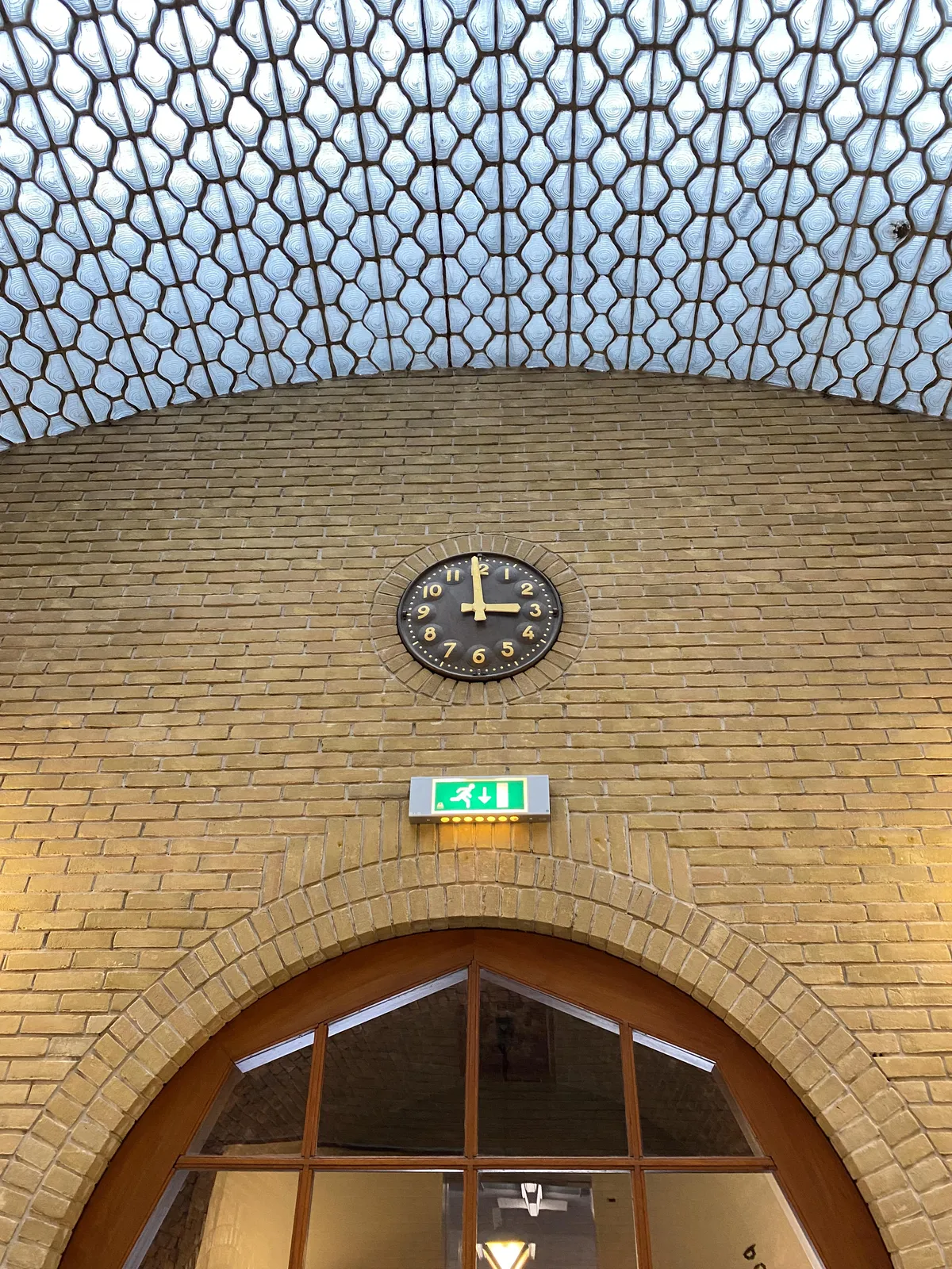 A clock, elaborately built into an arc shaped brick wall, above an arc shaped door. The clock points at 1 minute to three.