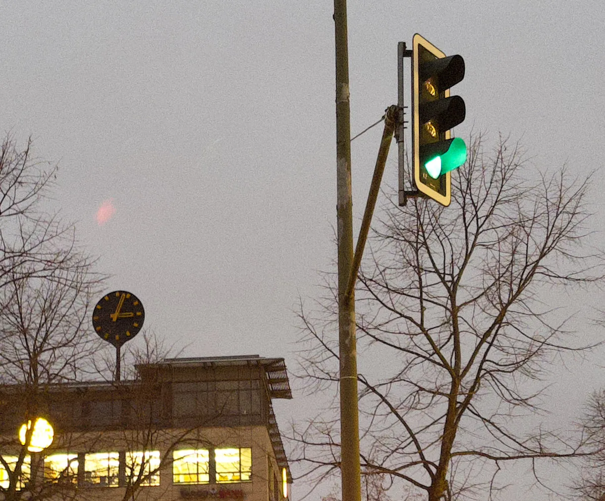 There’s a traffic light, which is green at the moment. There’s a wintery tree, without leaves. And in the background there’s a large clock on a large appartment building. It points at 3 minutes past 3.