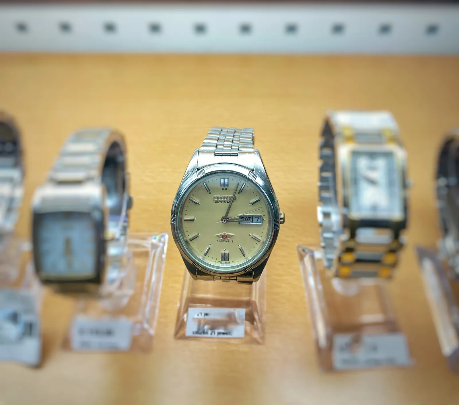 In this row of watches on display only the one in the middle is in focus. On its face it says it is a Citizen Automatic, 27 jewels watch. It points at 3 minutes past 3.