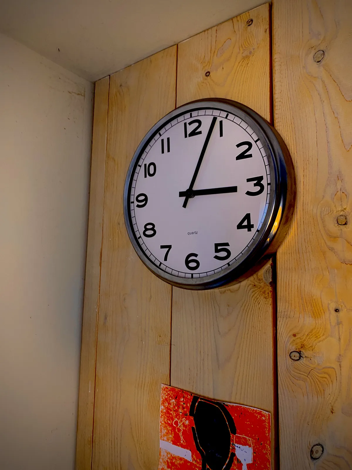 A clock on a wooden wall points at 3 minutes past 3.