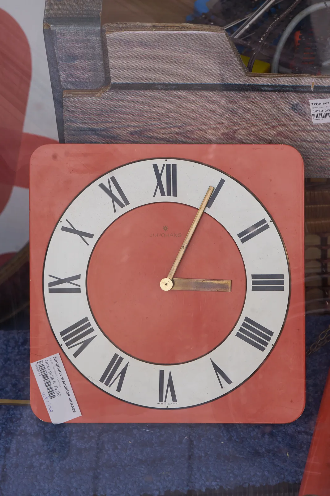 The golden pointers on this orange clock say it’s four minutes past three.