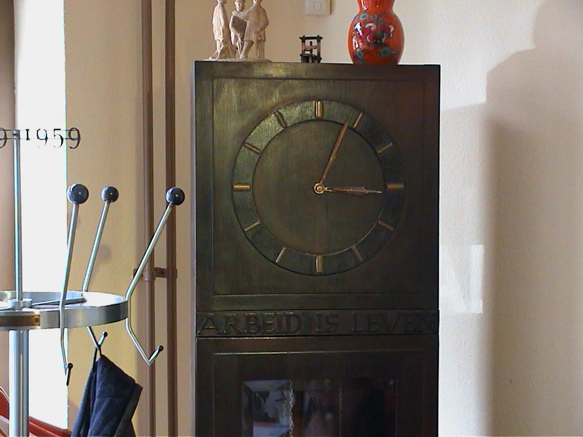 An old wooden clock (with the words Arbeid is Leven on it) points at four minutes past three.