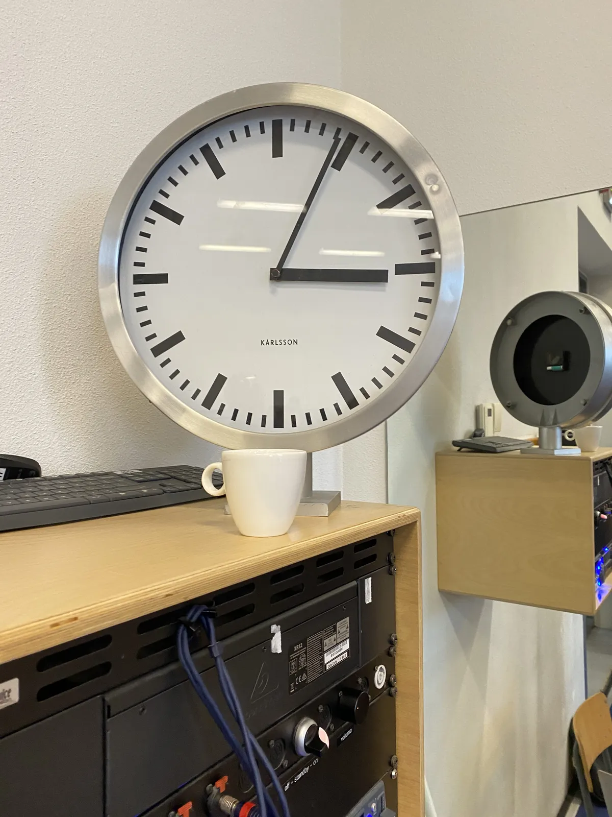 There’s a keyboard, some electrical equipment with wires and knobs and a modern clock. Behind the clock there’s a mirror so you can see the back of it, which is not noteworthy. The clock points at 4 minutes past 3.   
