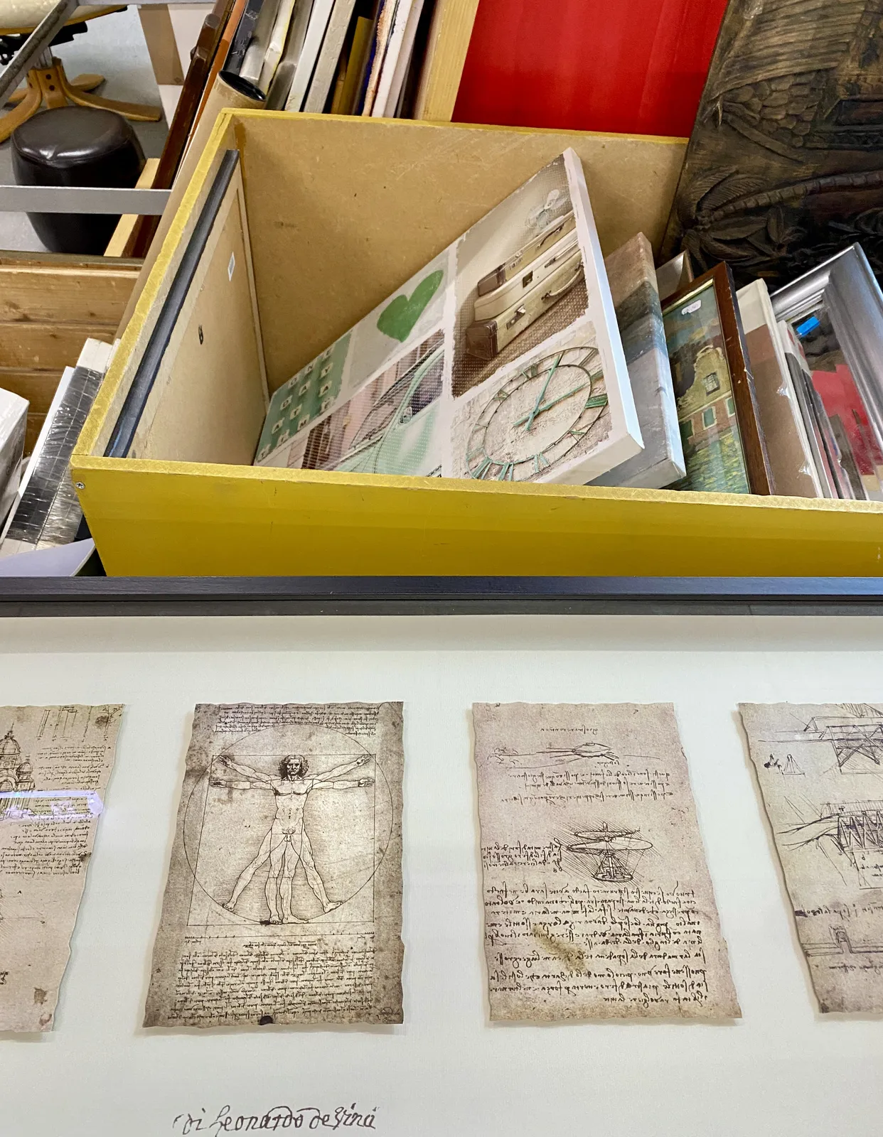 Drawings and prints for sale at a thirft shop. On one of the prints there’s a clock which points at 5 past 3.