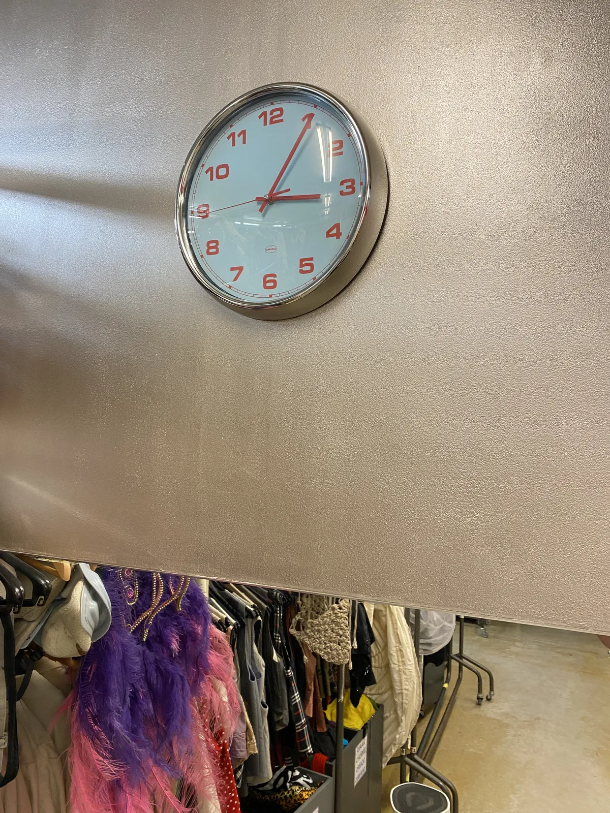 Peeking down to a wardrobe full of theatrical clothing. On the wall there’s a clock which points at 5 past 3.