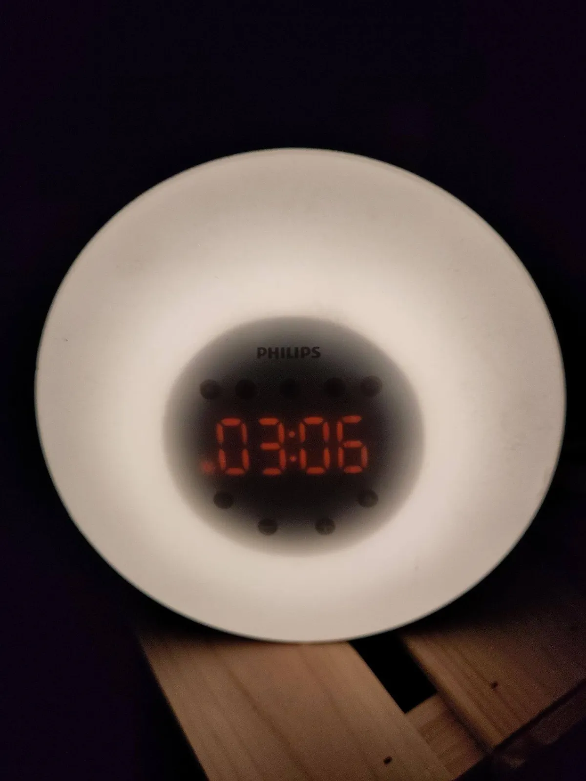 A digital clock with red digits, surrounded by something that looks like a white plastic cap. The clock says it is 03:06