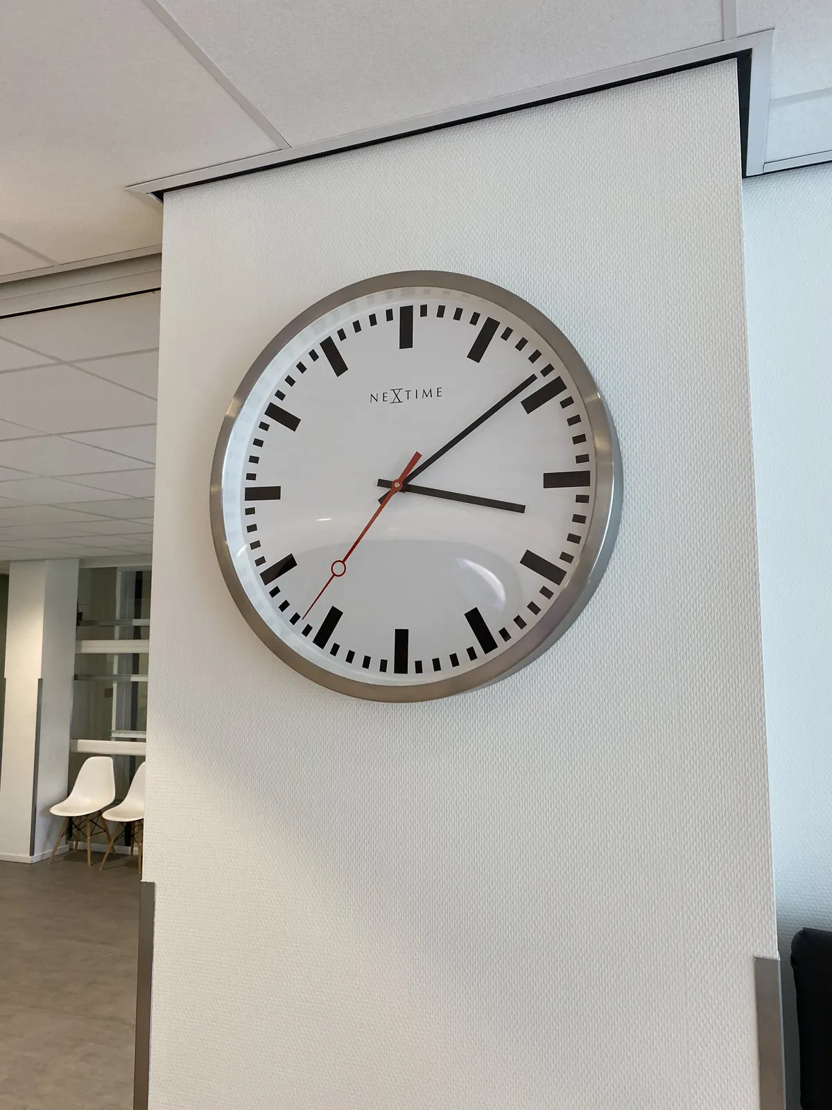 A modernist clock on a wall. It points at 9 past 3.