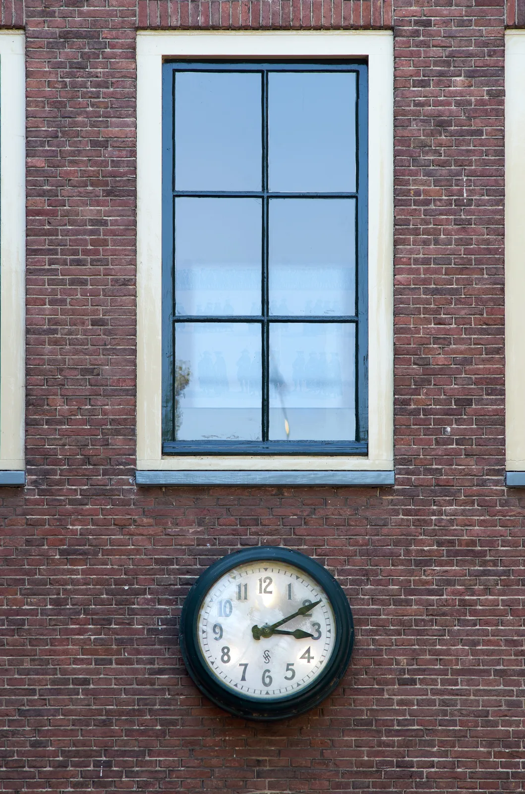 On a old brick wall, below a window, there’s an old clock. It points at 10 past 3.