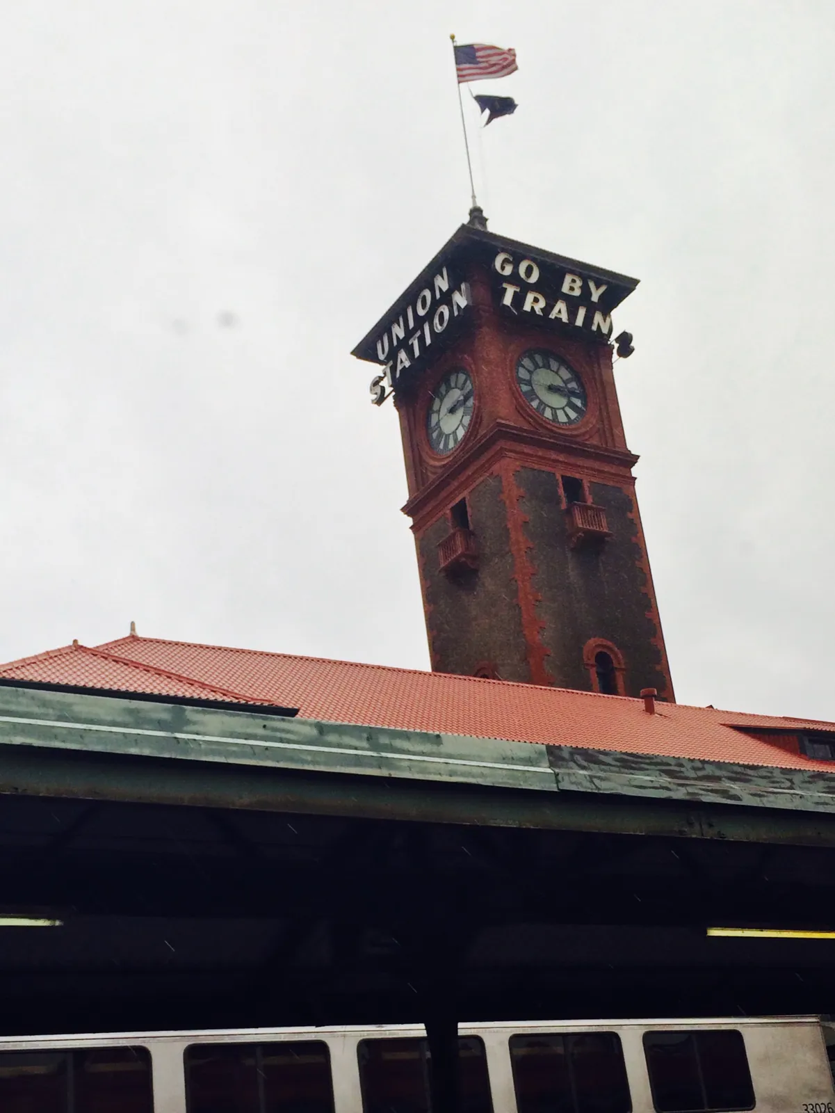 A red roof with a tower on it with a US flag, and a message that says this is a Union station and which urges you to go by train. The clock on this tower points at 13 minutes past 3.
