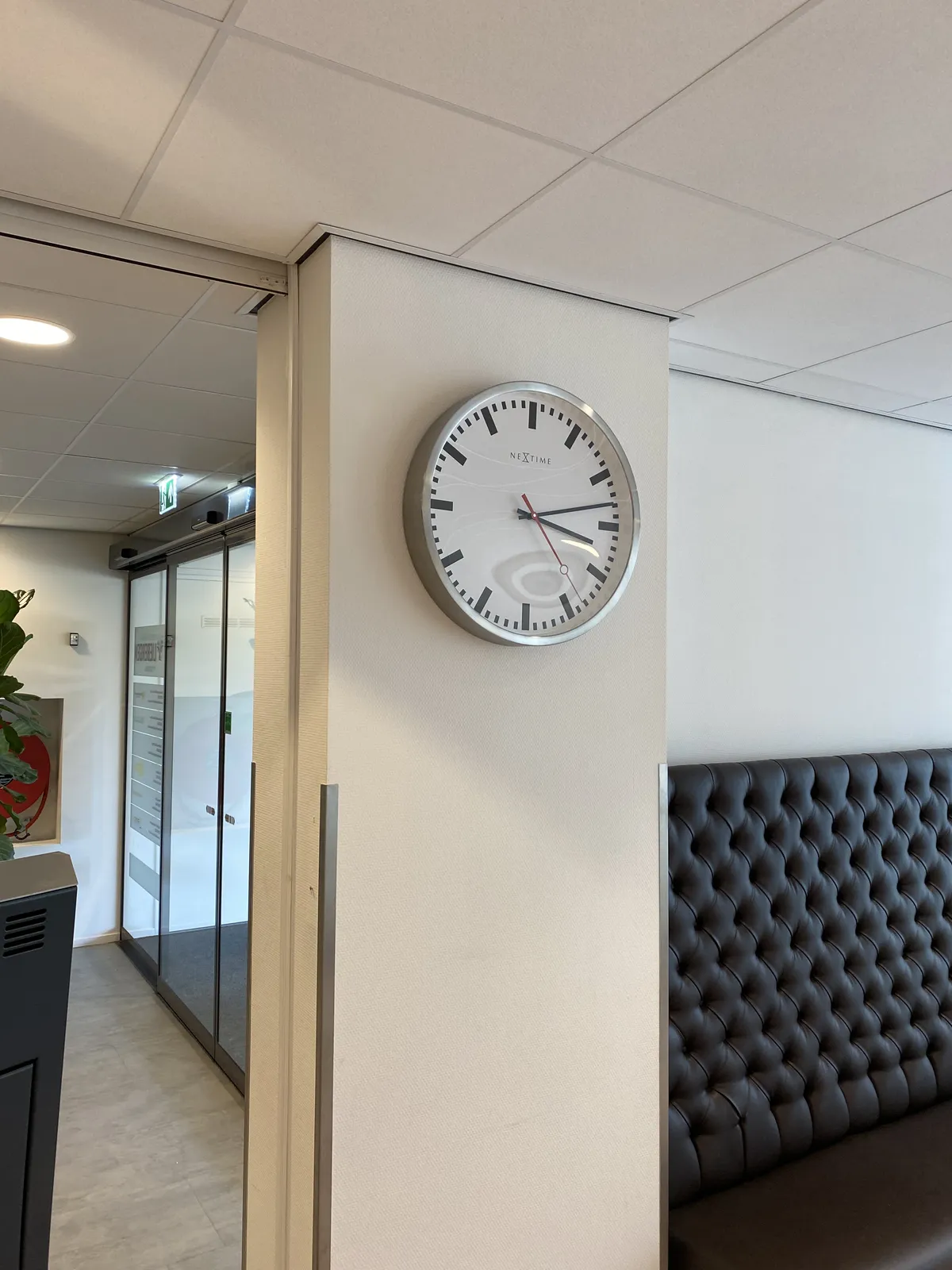 A modernist clock on a wall. It points at 13 past 3.