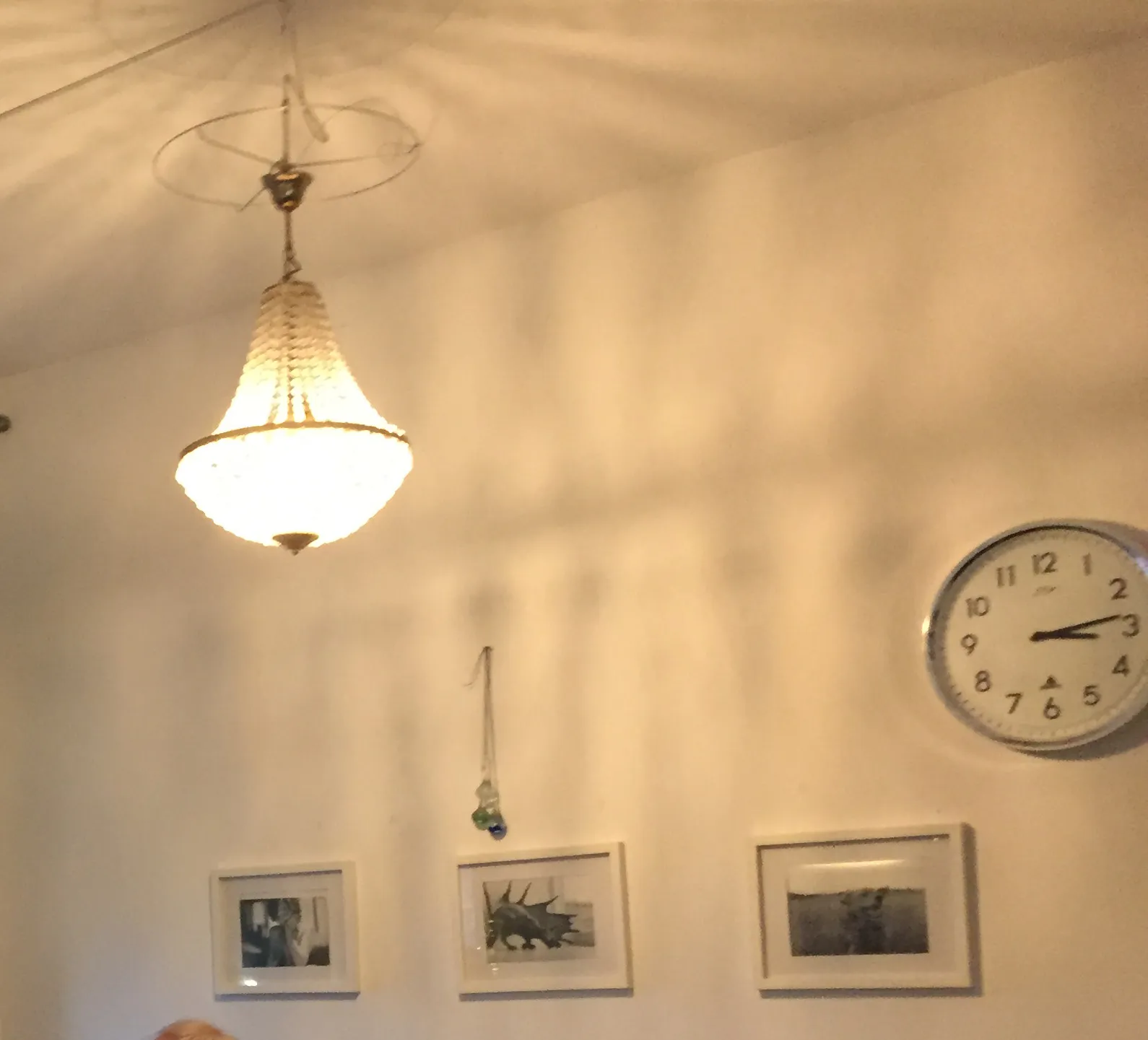A chandelier, three framed black and white photos on the wall, next to a clock. According to this clock it is 14 past 3. 