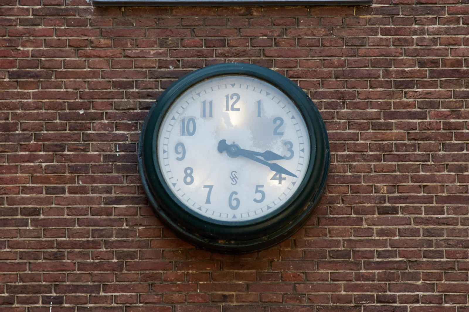 On a brick wall there’s an old clock. It has a nice little logo on it made from the letters S and H. It points at 19 past 3.