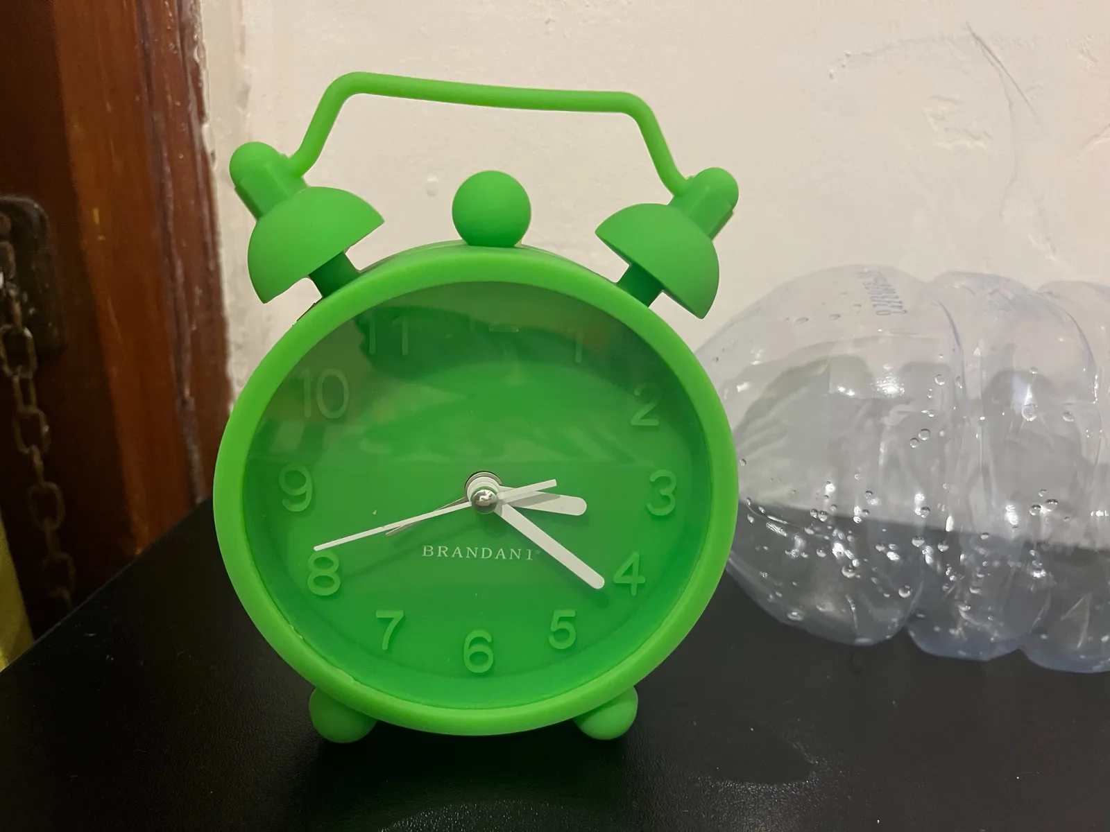 A green, fully plastic clock in the shape of an old fashioned alarm clock. It points roughly at 21 minutes past 3.