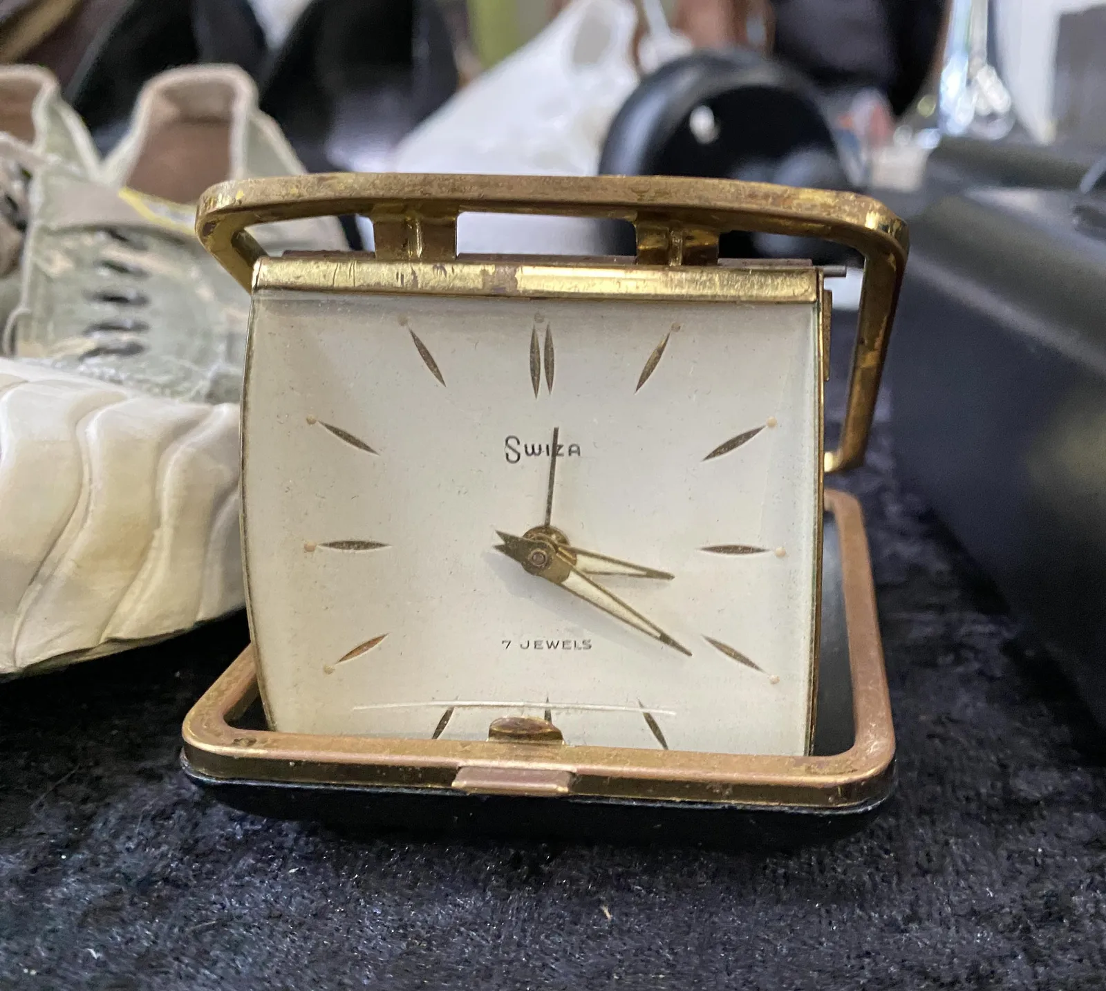 A small, old, silver travel clock on a flea market. The words Swiza and 7 jewels are printed on its face. It points at 21 minutes past 3.