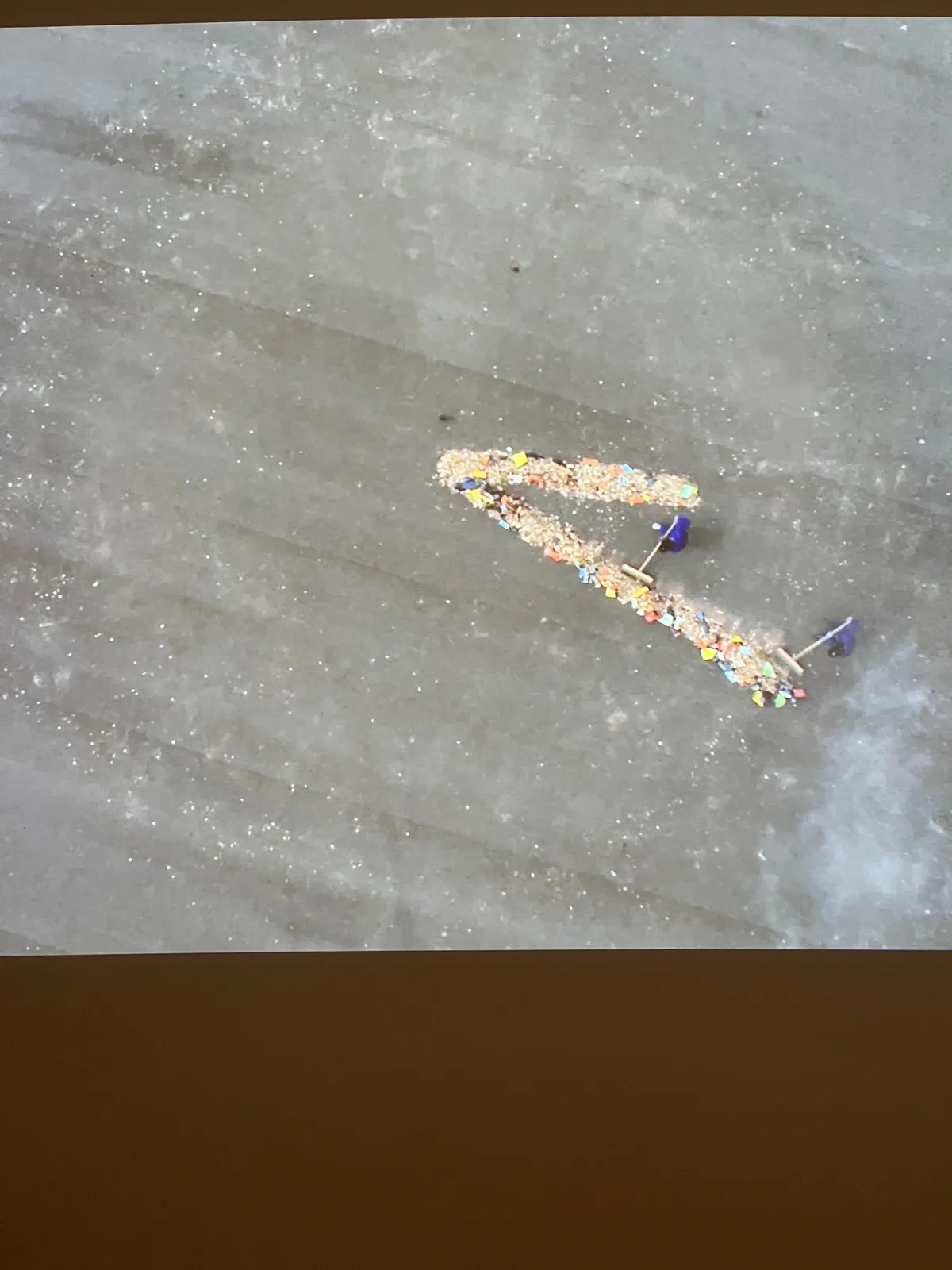 Filmed from above, two people are sweeping rubbish in the shape of hands of a clock. This shape gives us the idea that it is 22 past 3.