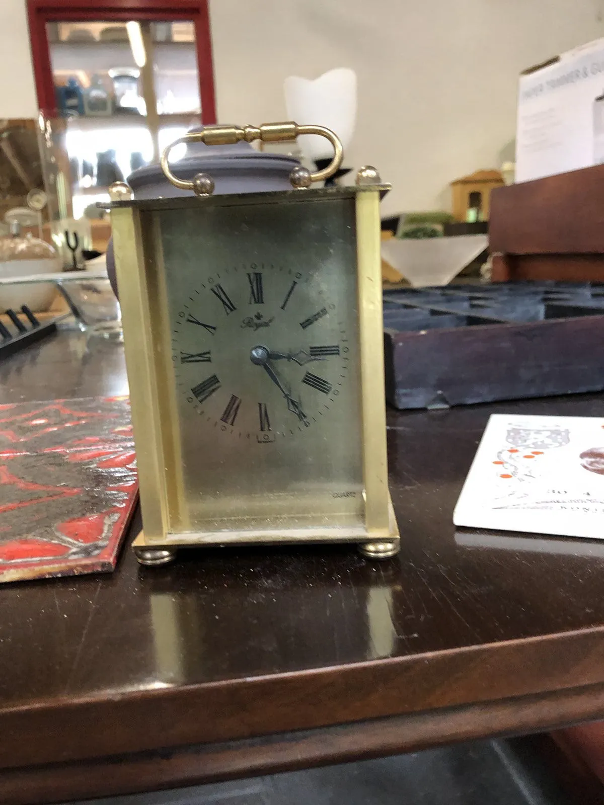 A little metal clock standing on a table. It points at 24 past 3.