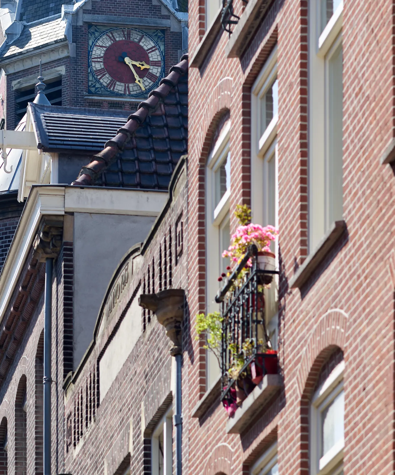 Behind the facade of some Amsterdam houses a church clock points at 25 past 3.