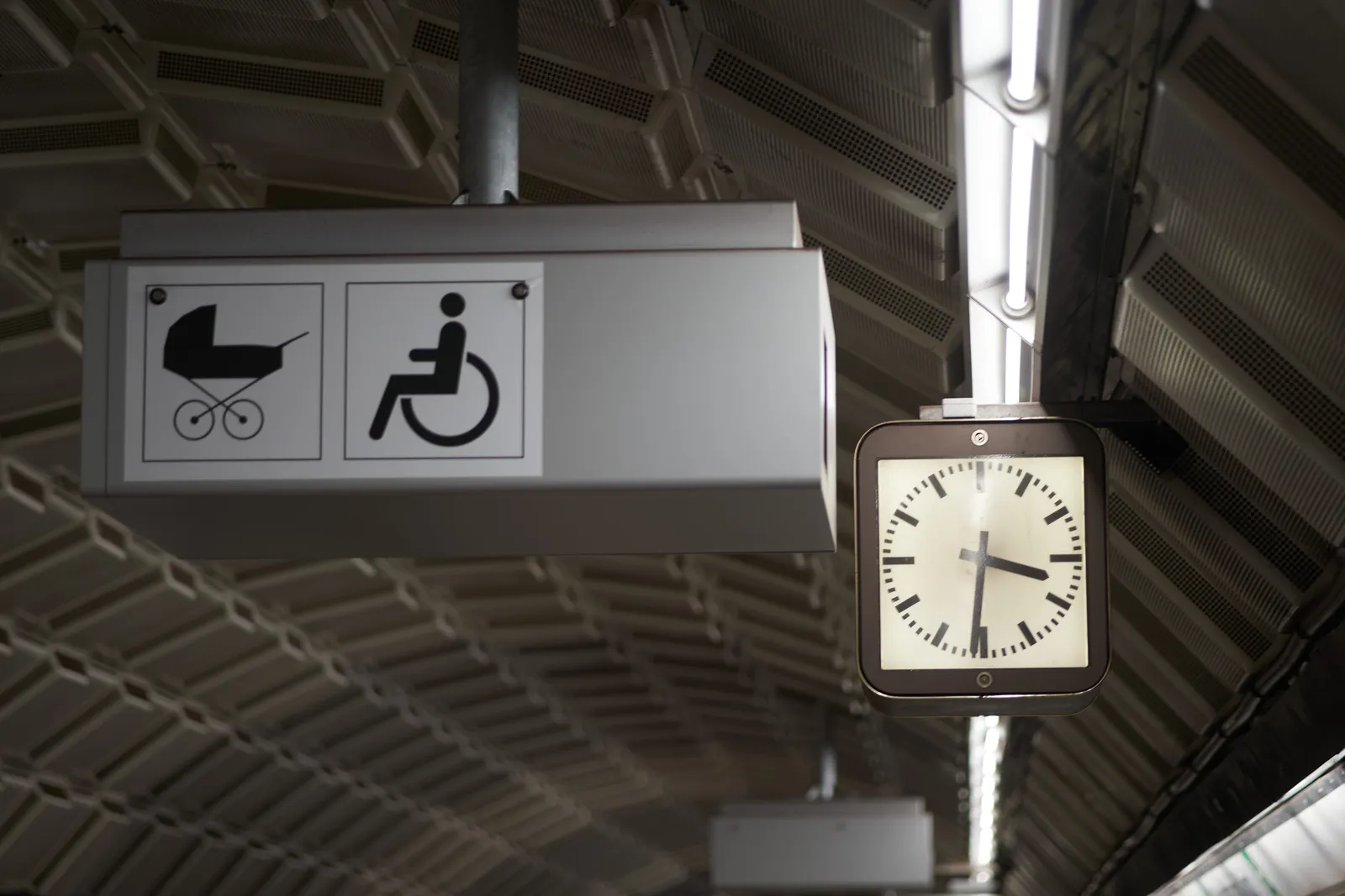 A clock in a tunnel, next to a sign with a baby buggy and a wheel chair. The clock points at 29 minutes to 4.