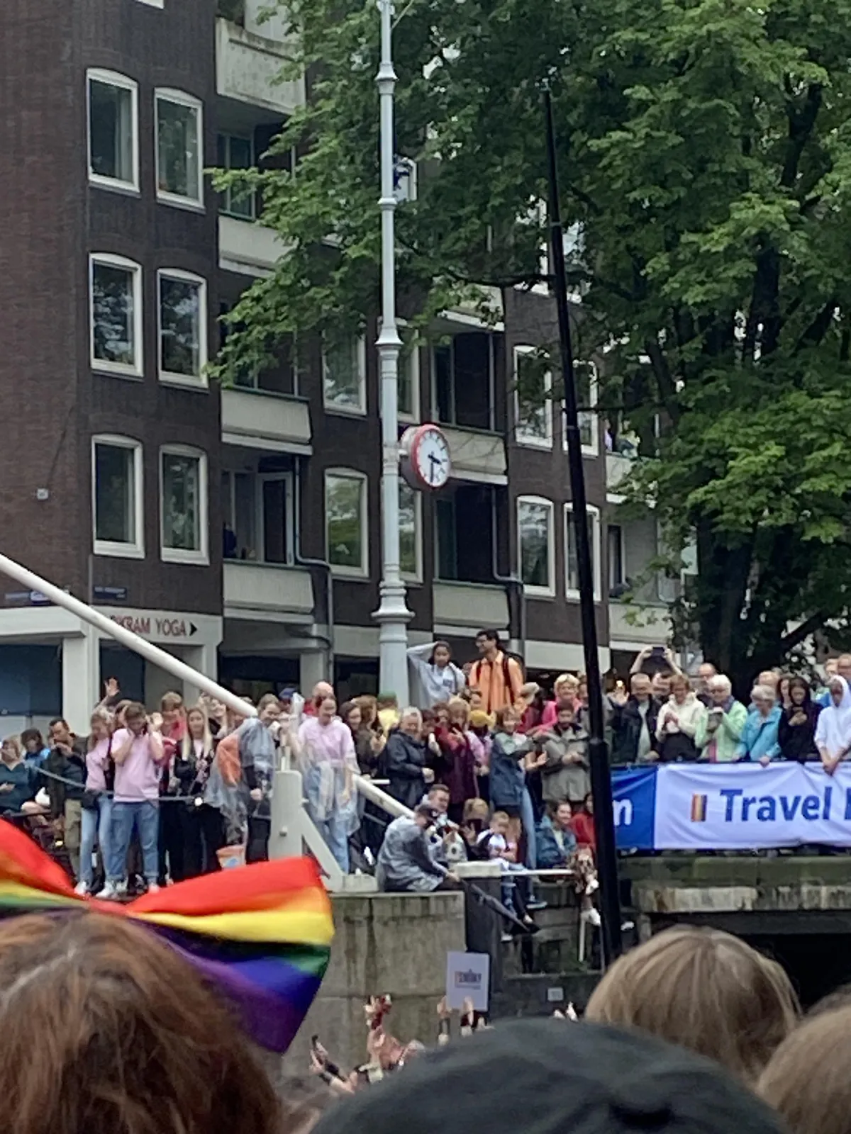 Many people standing next to the canals during the gay pride in Amsterdam. There’s also a clock in this picture which points at 31 minutes past 3.