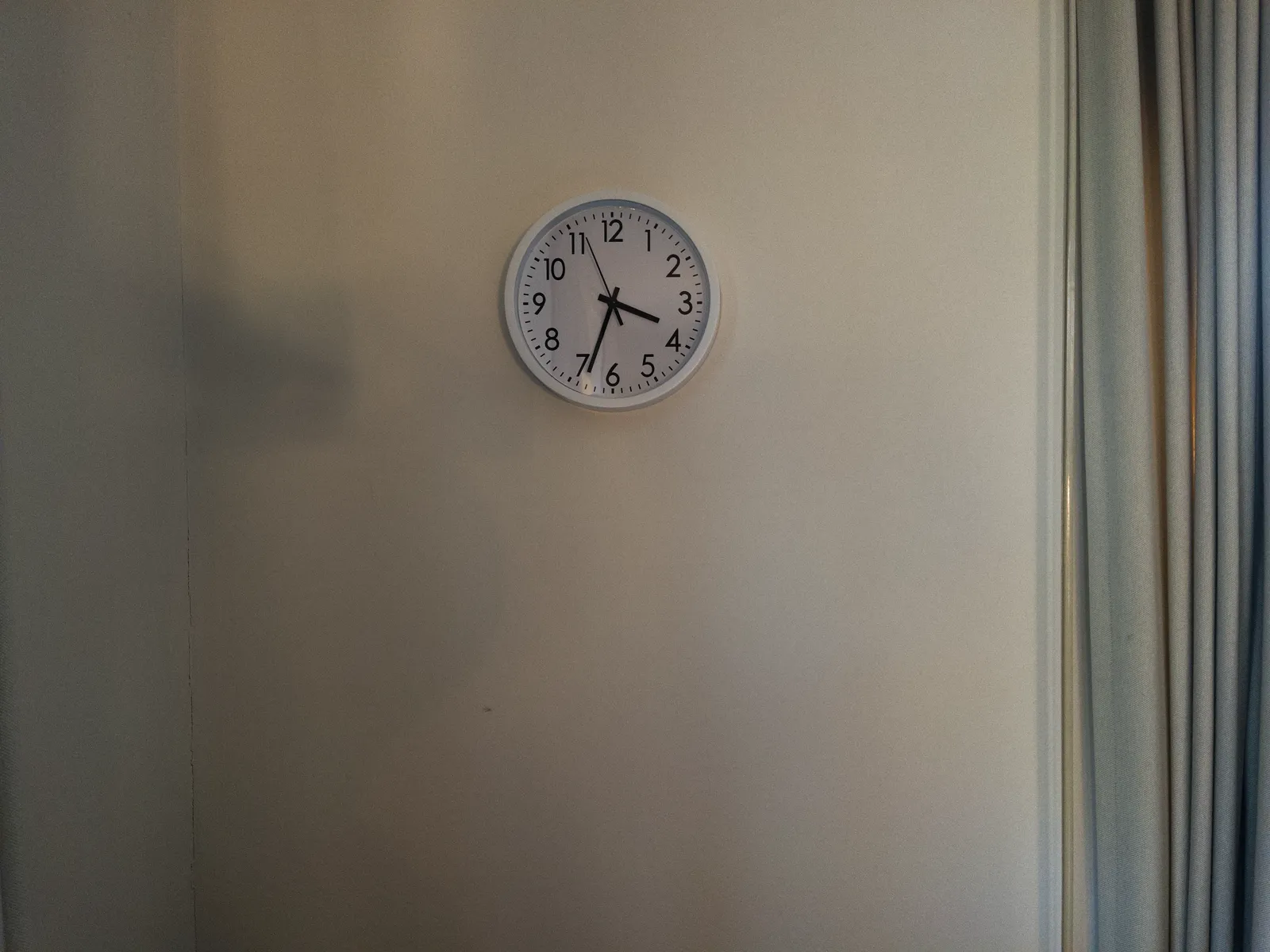 A simple wall clock on a white wall. It points at 33 minutes past three.