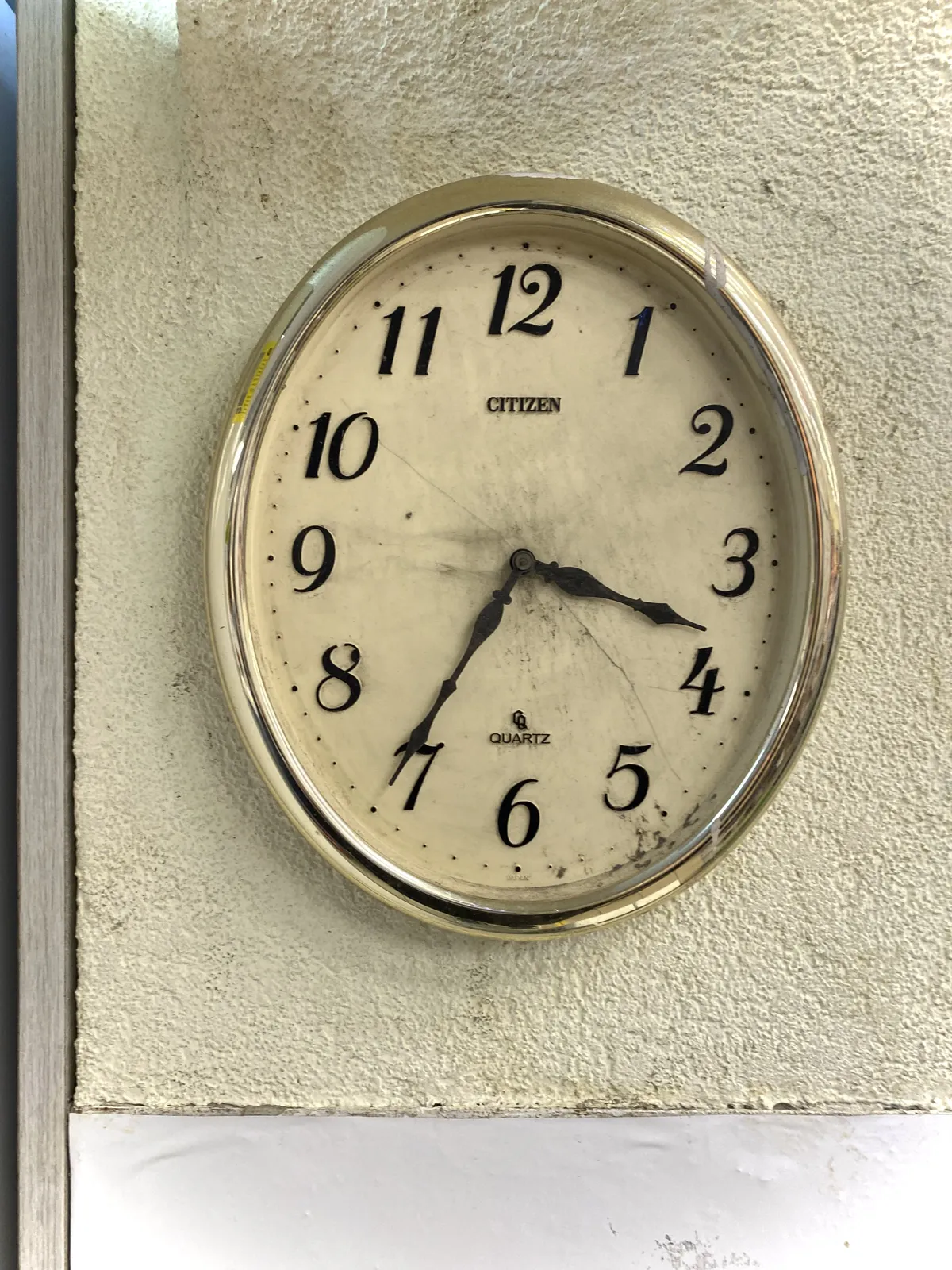 An oval wall clock with the words Citizen Quartz printed in its face points at 25 minutes to 4.