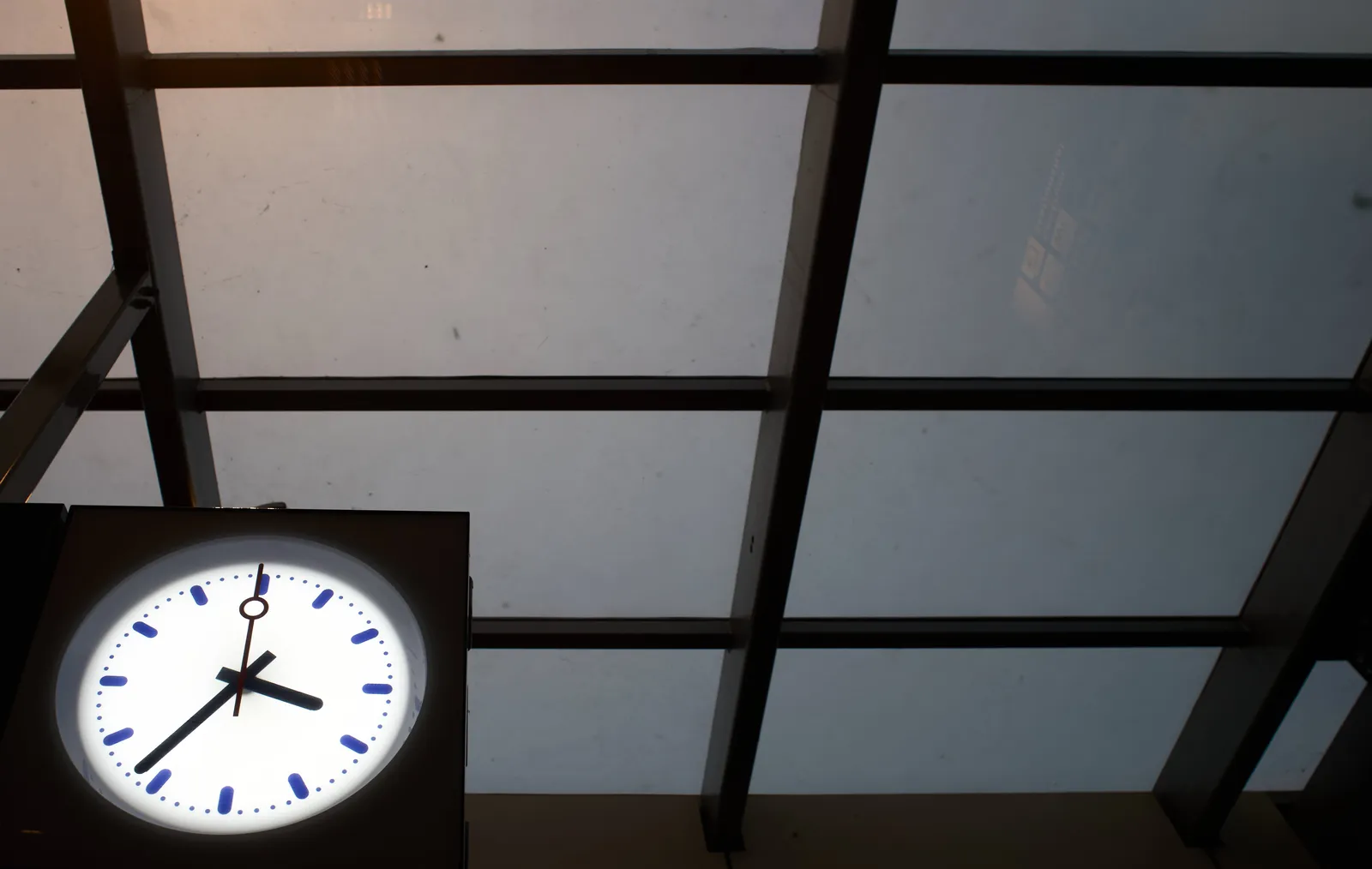 In the background there’s a black construction grid against a gray roof. In the bottom left corner of the picture there’s a clock that points at 36 minutes past 3. 