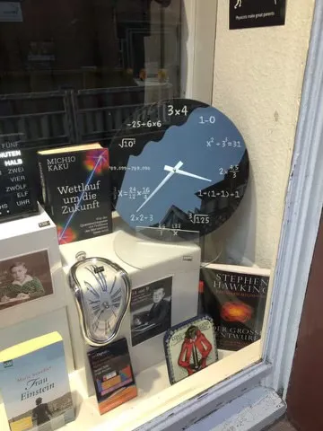 A black clock in the window of a book store. The hour indicators are replaced by complicated mathematical equations. It points roughly at 36 minutes past 3.