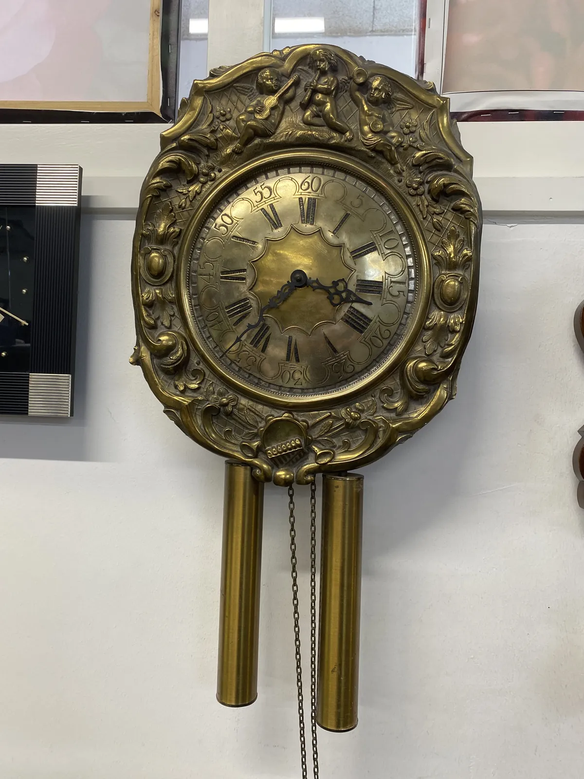 A clock made from metal, ornamented with little music playing cherubs. The hands point at 23 minutes to 4.