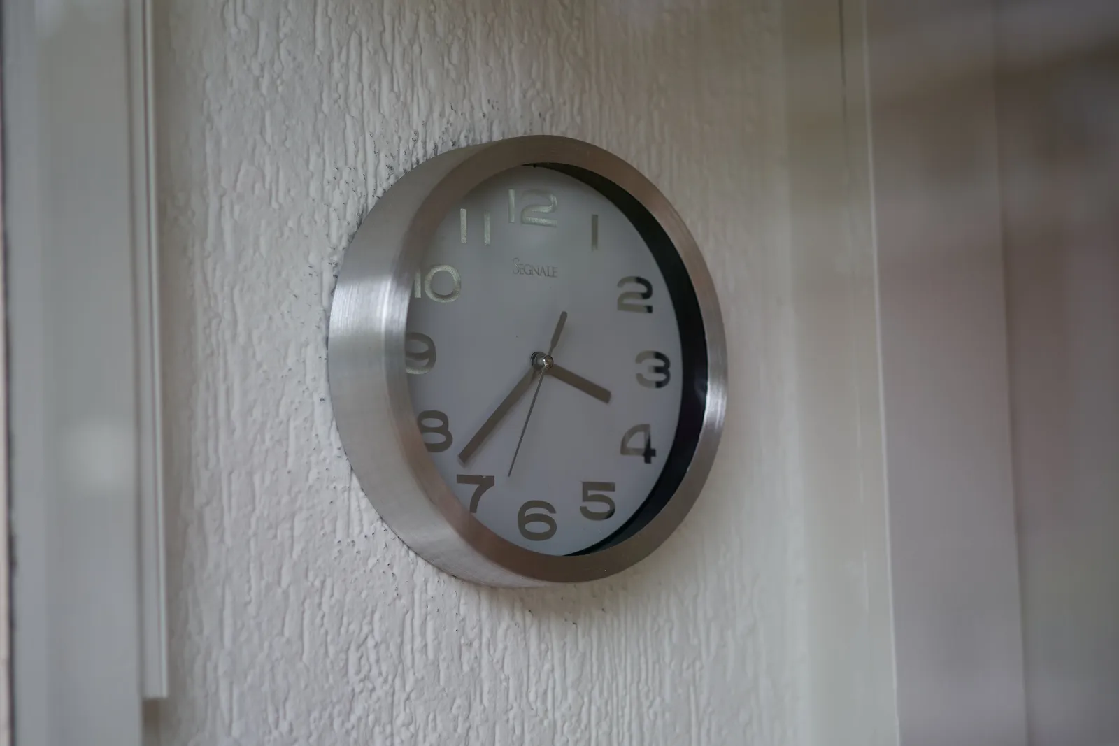 A clock on a wall. It points at 23 minutes to 4.