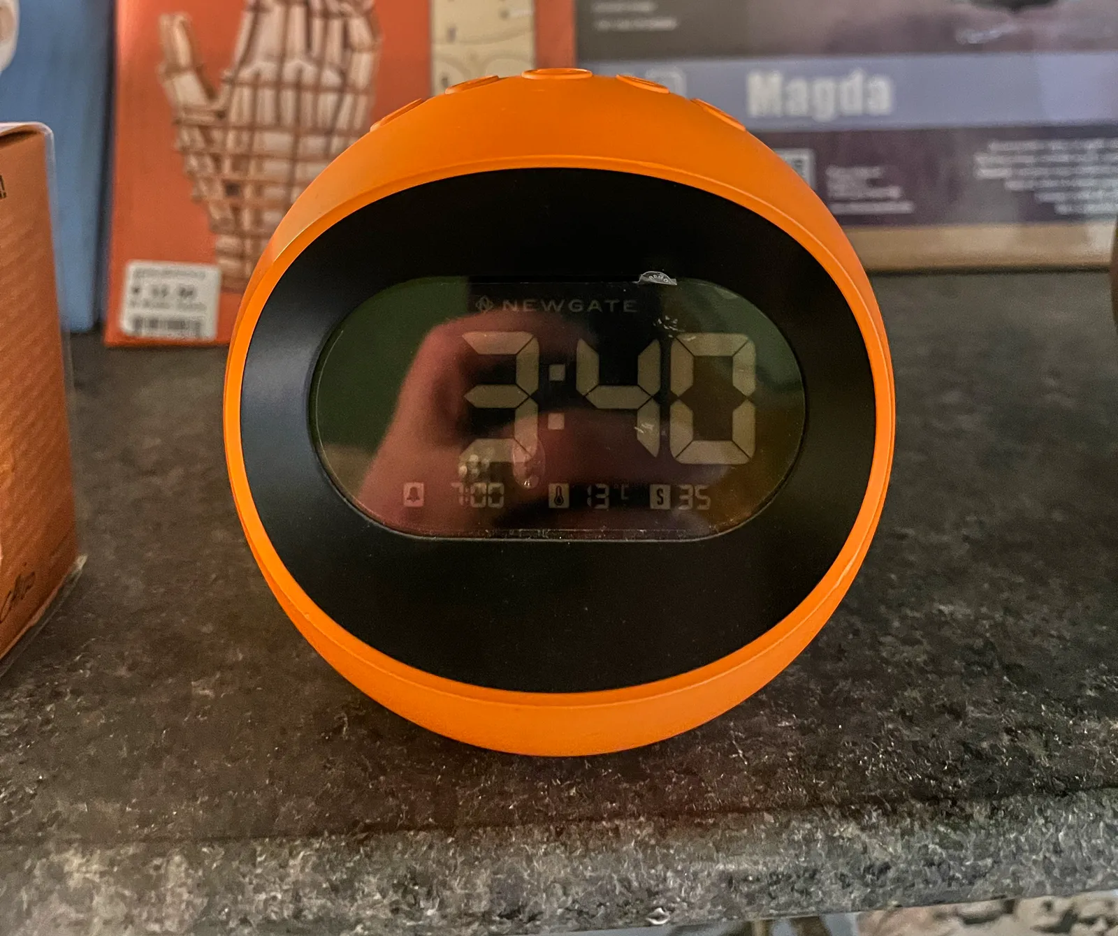 A clock in the shape of a bright orange ball. In the digital display it says 3:40
