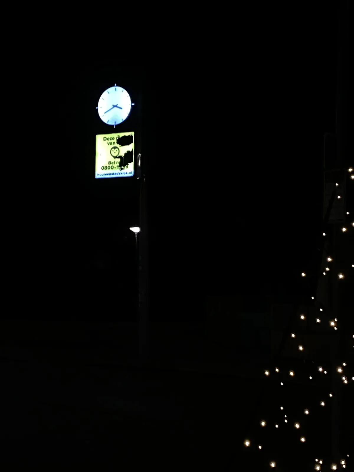 A mostly black picture. There are some lights from a christmas tree in one corner. There’s also a street light. And there is a clock that points at 19 minutes to 4.