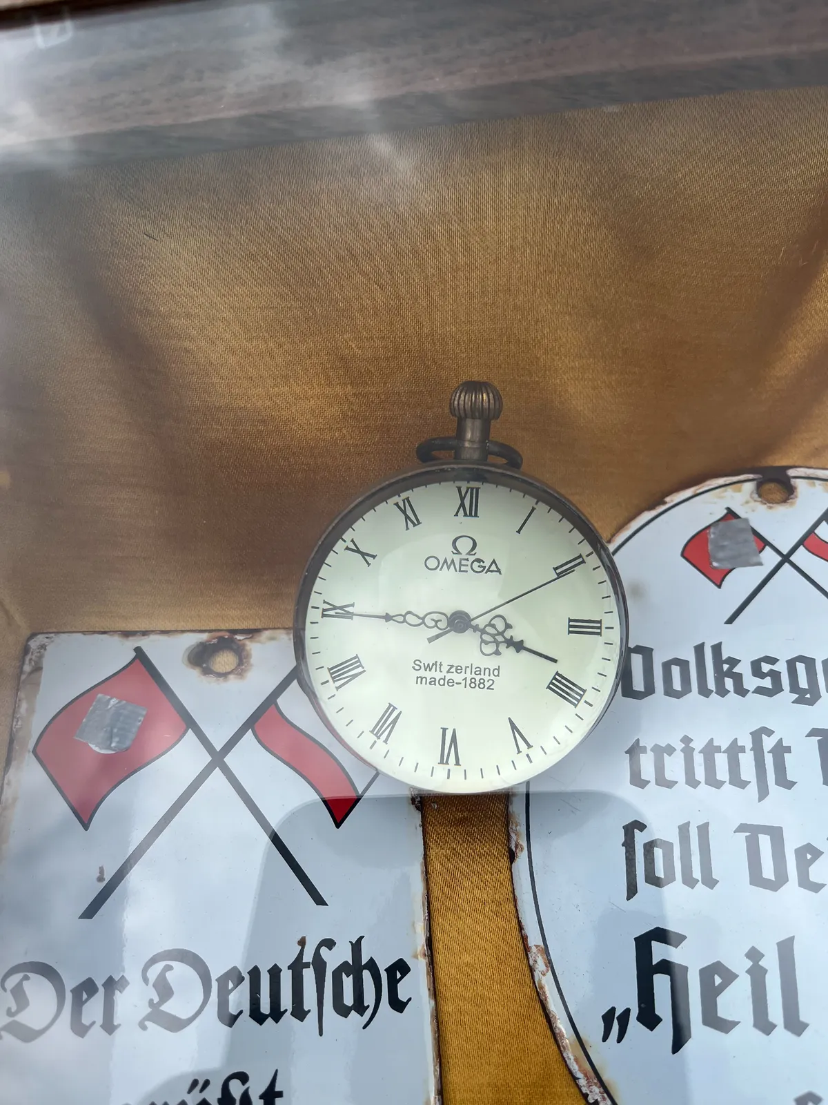 A nice, old clock lies amids some nazi paraphernalia. The clock says Omega, and Switzerland made 1882 on its face. It points at a quarter to 4.