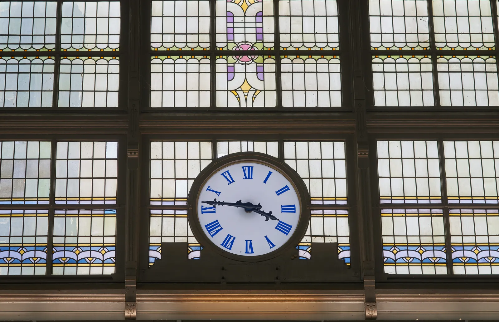 An old clock fitted in a stained window points at 14 minutes to four. 