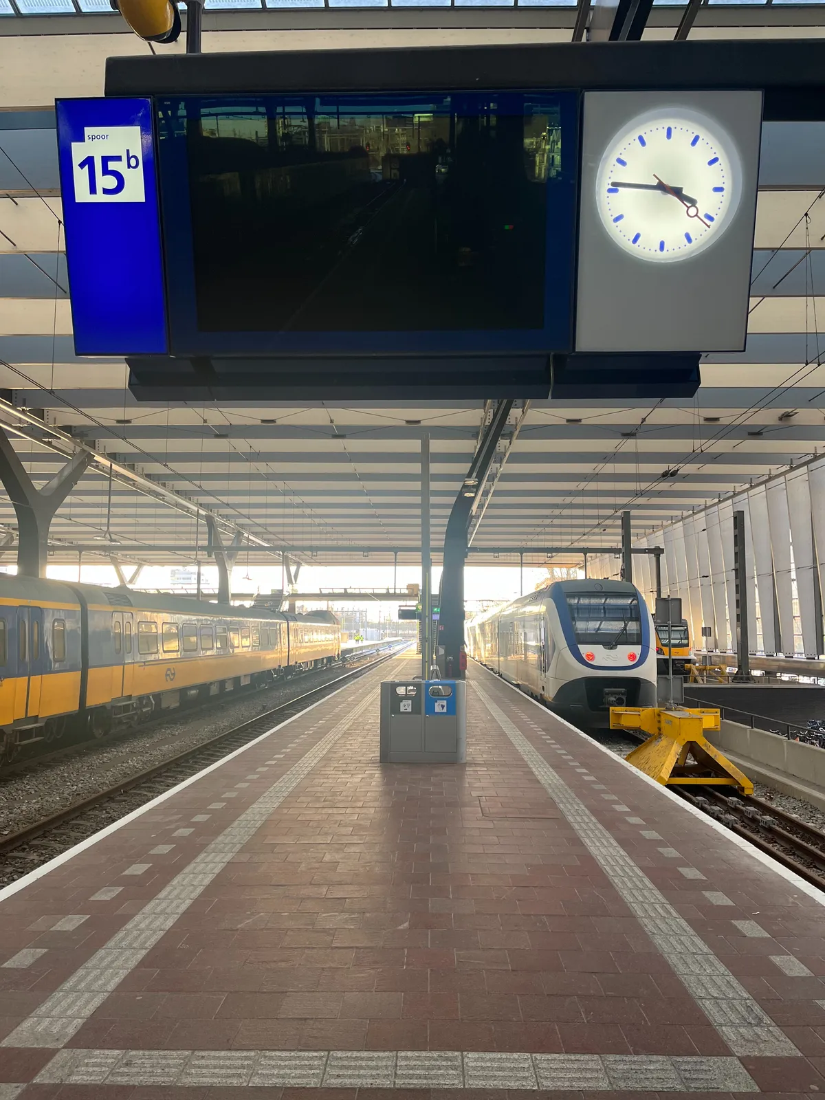 Trains on a station and an empty display on platform number 15. The clock attached to this display shows the time as 14 minutes to 4.