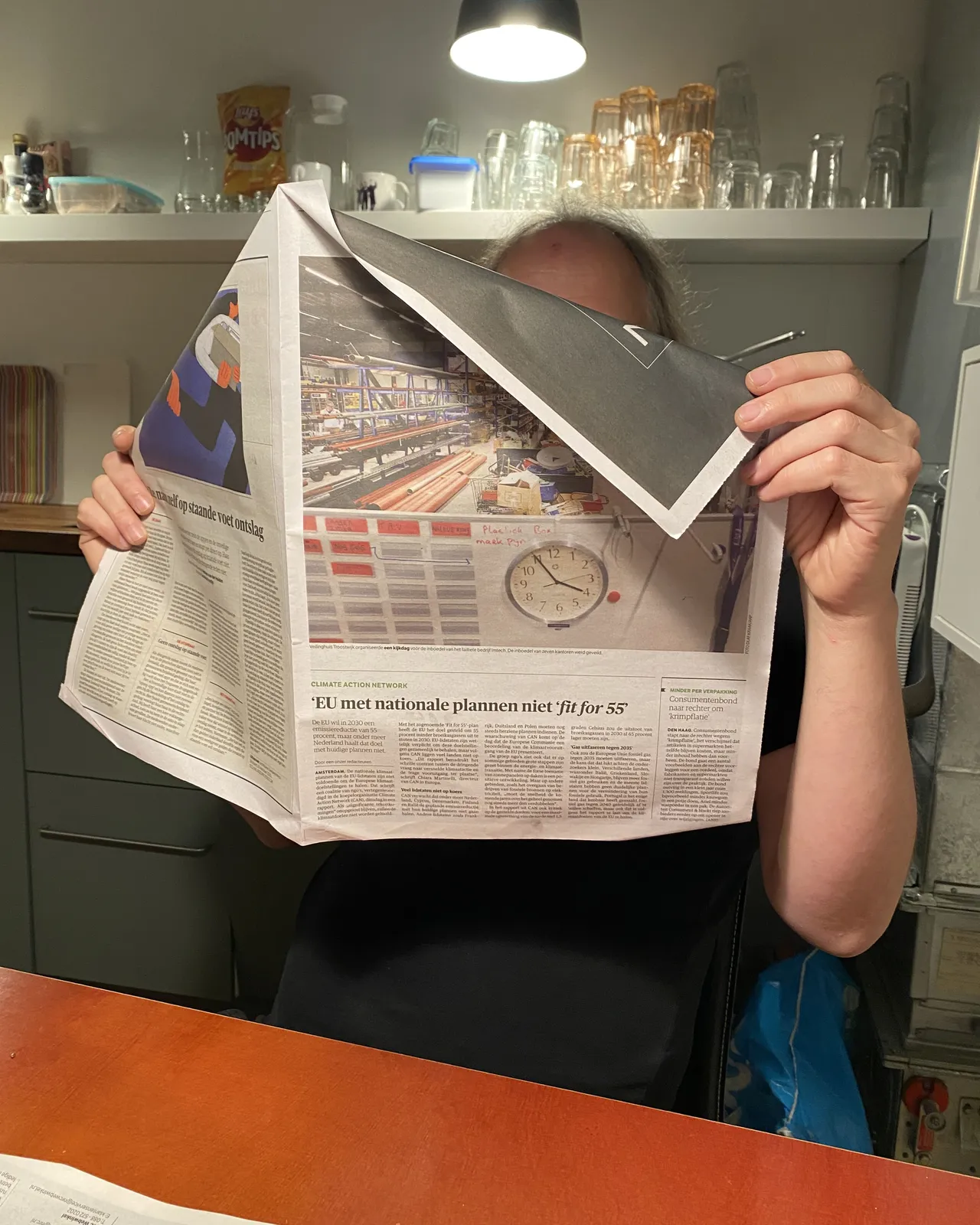 Someone is reading the newspaper. There’s a clock printed on it which points at 5 minutes to 4. 