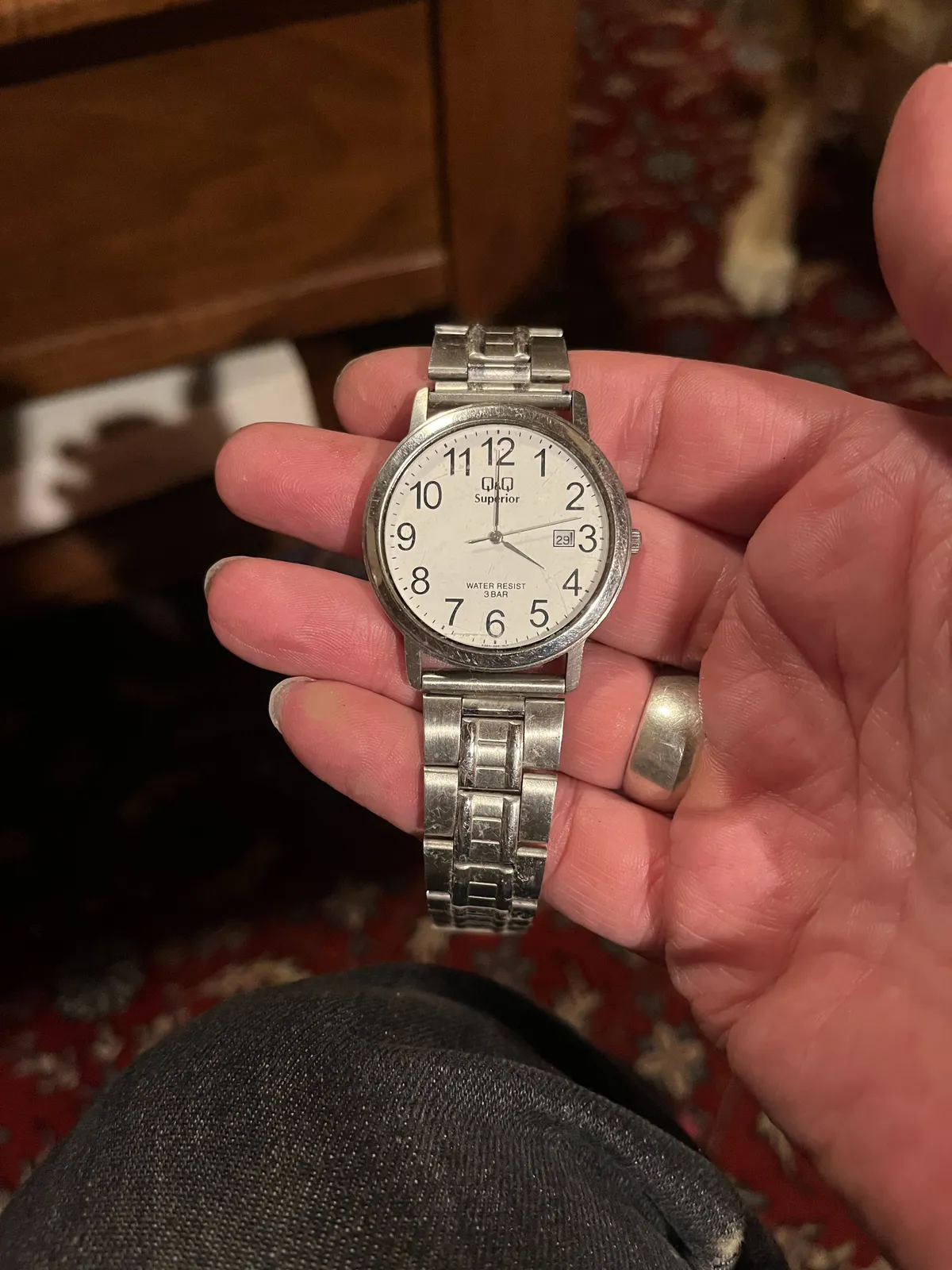 Someone is holding an old watch in their hand. In the background, blurry, an old Persian rug. The watch points at four o’clock.