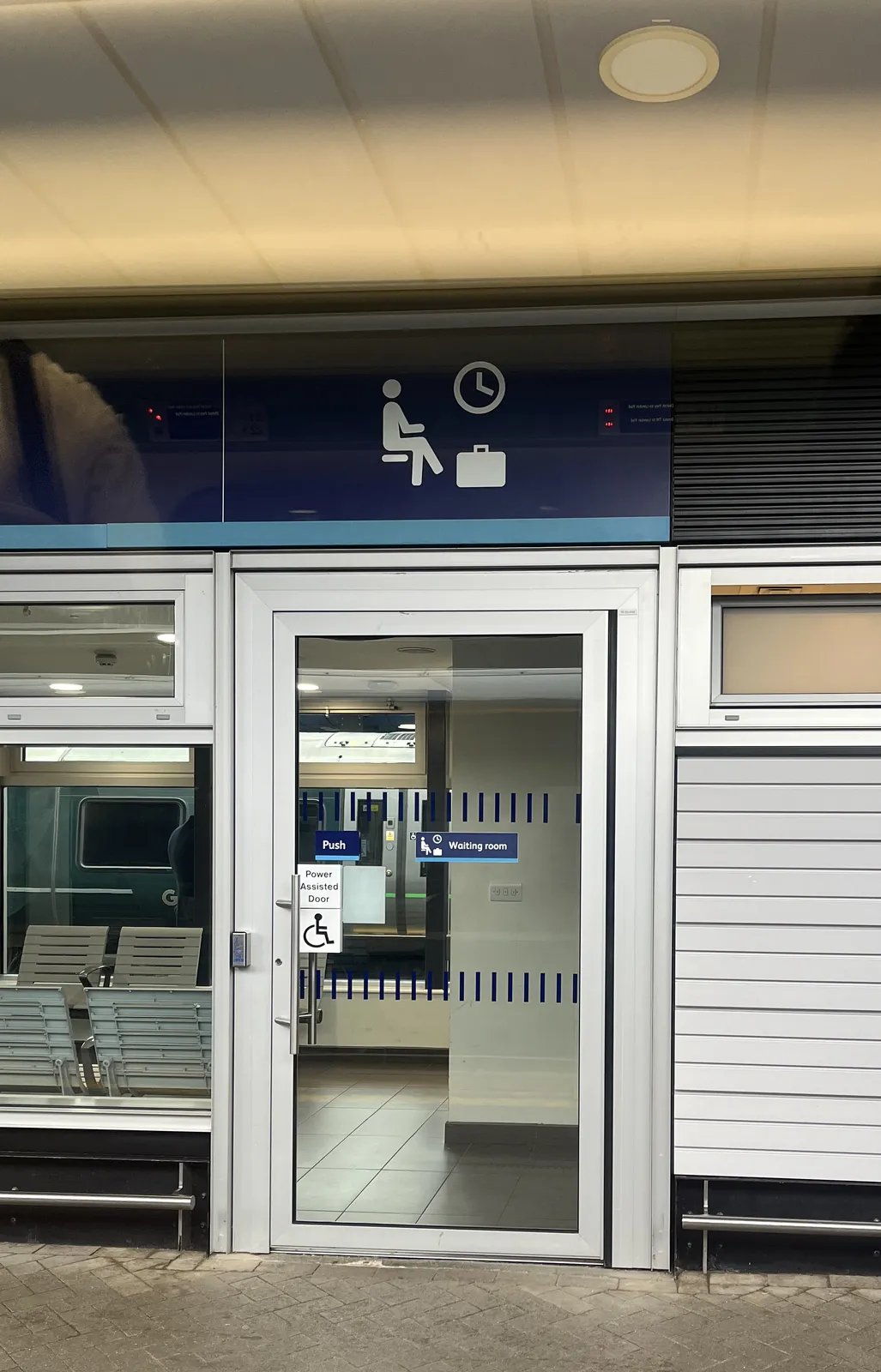 A glass door, with some icons above it that might indicate that this is a waiting room. One of the icons is an icon of a clock, which points at four o’clock. 