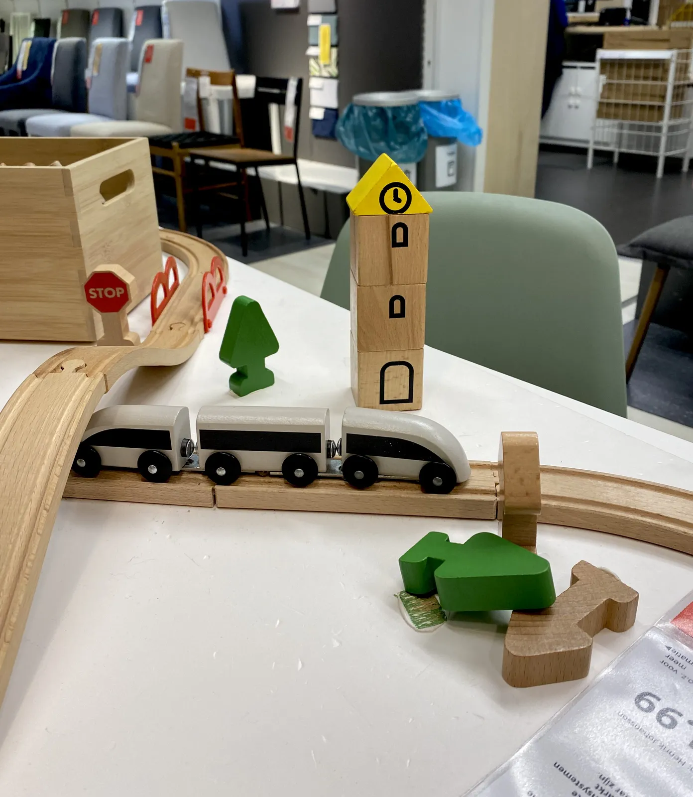 A wooden toy train, with wooden tracks, and wooden trees, on a table in a thrift store. There’s also a wooden tower with a clock painted on it. It points at 4 o’clock.