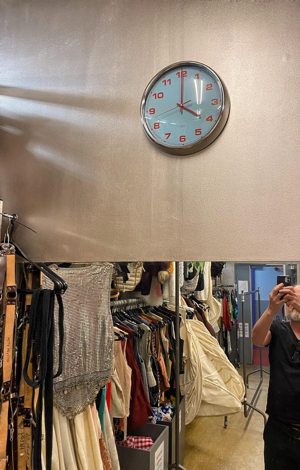 In a clothing shop, above a large mirror there’s a clock which points at 4 o’clock. In the mirror the photographer can be seen.