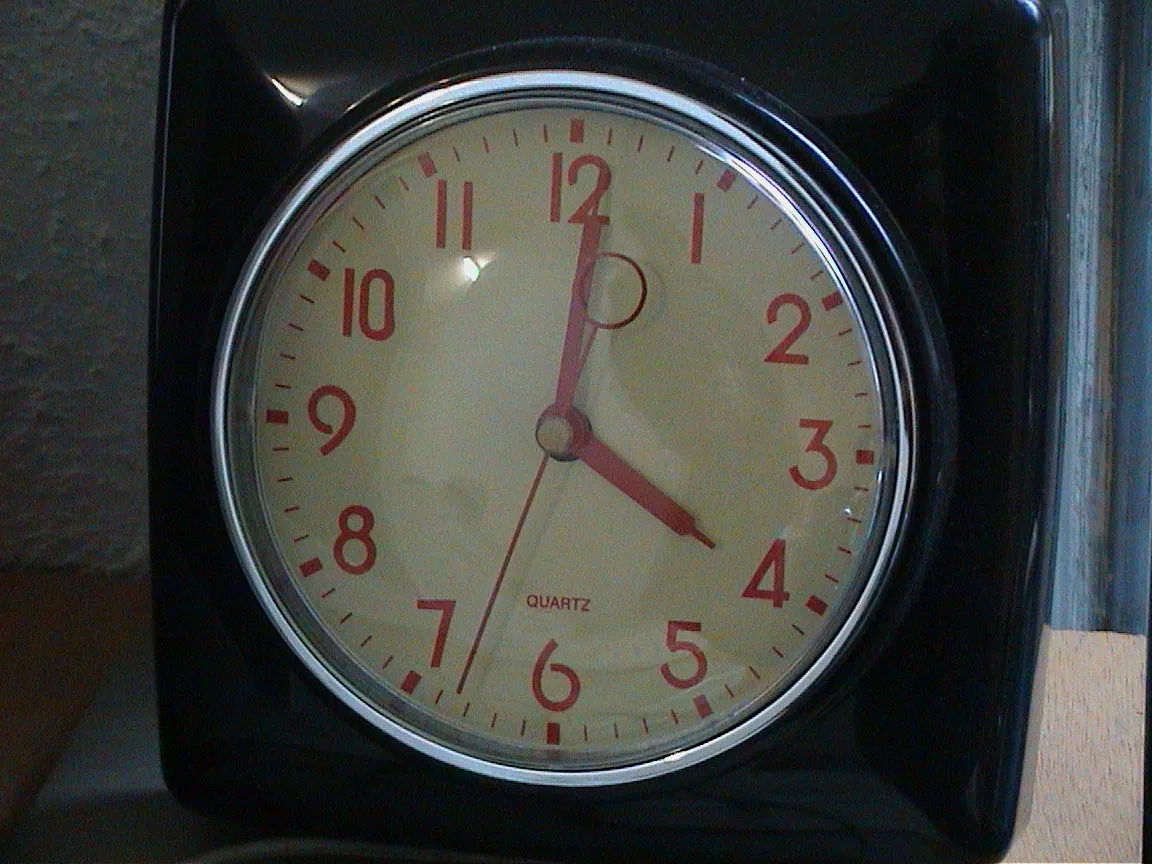 A clock with orange numbers shows the time is one minute past four.