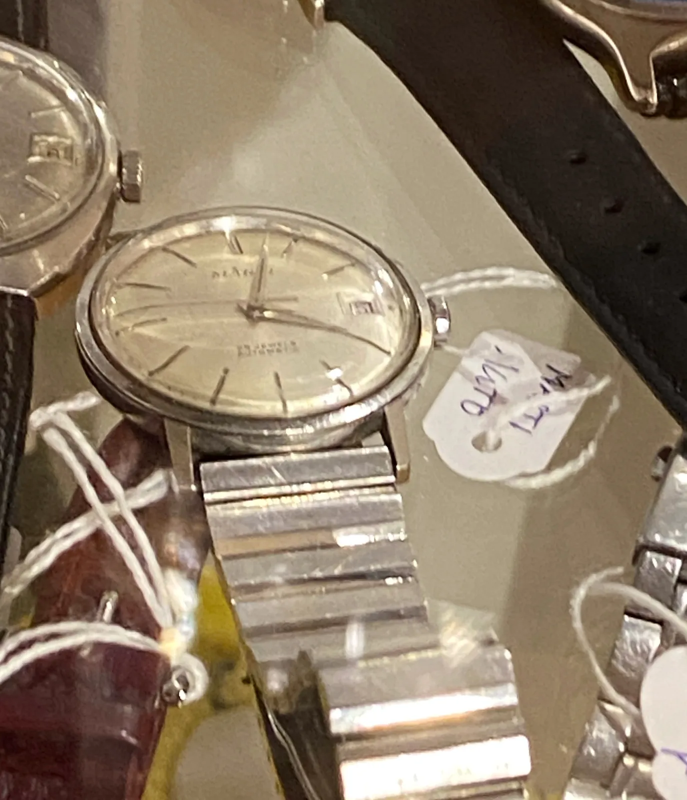 A few wrist watches on a glass plate. Just one of them is clearly in focus. It points at two minutes past 4.
