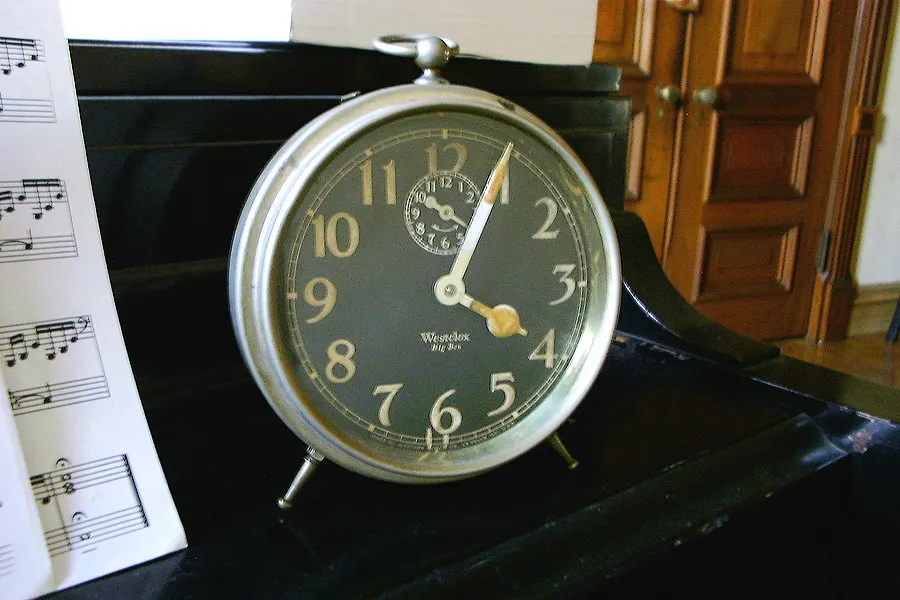 A clock standing on a piano says it is 4 minutes past 4.