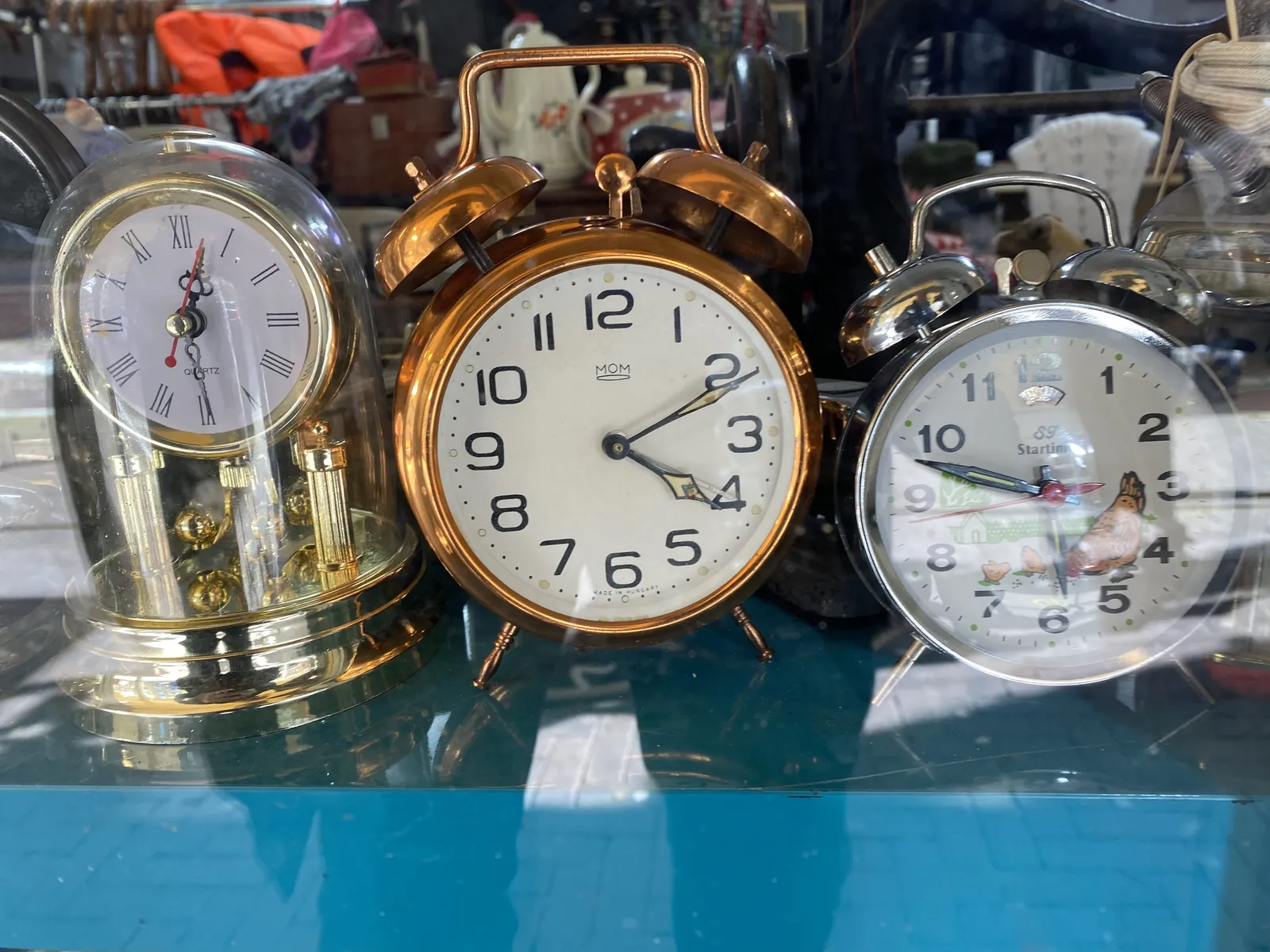 There are three old alarm clocks in this picture. The one in the middle, which is made of copper-like metal, points at 11 past 4.