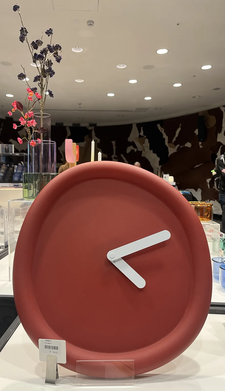 A clay red clock. It has no indicators at all, so in that sense it is minimalist. But it is deliberately not perfectly round, not at all. It has to white hands that point at approximately 11 minutes past four.