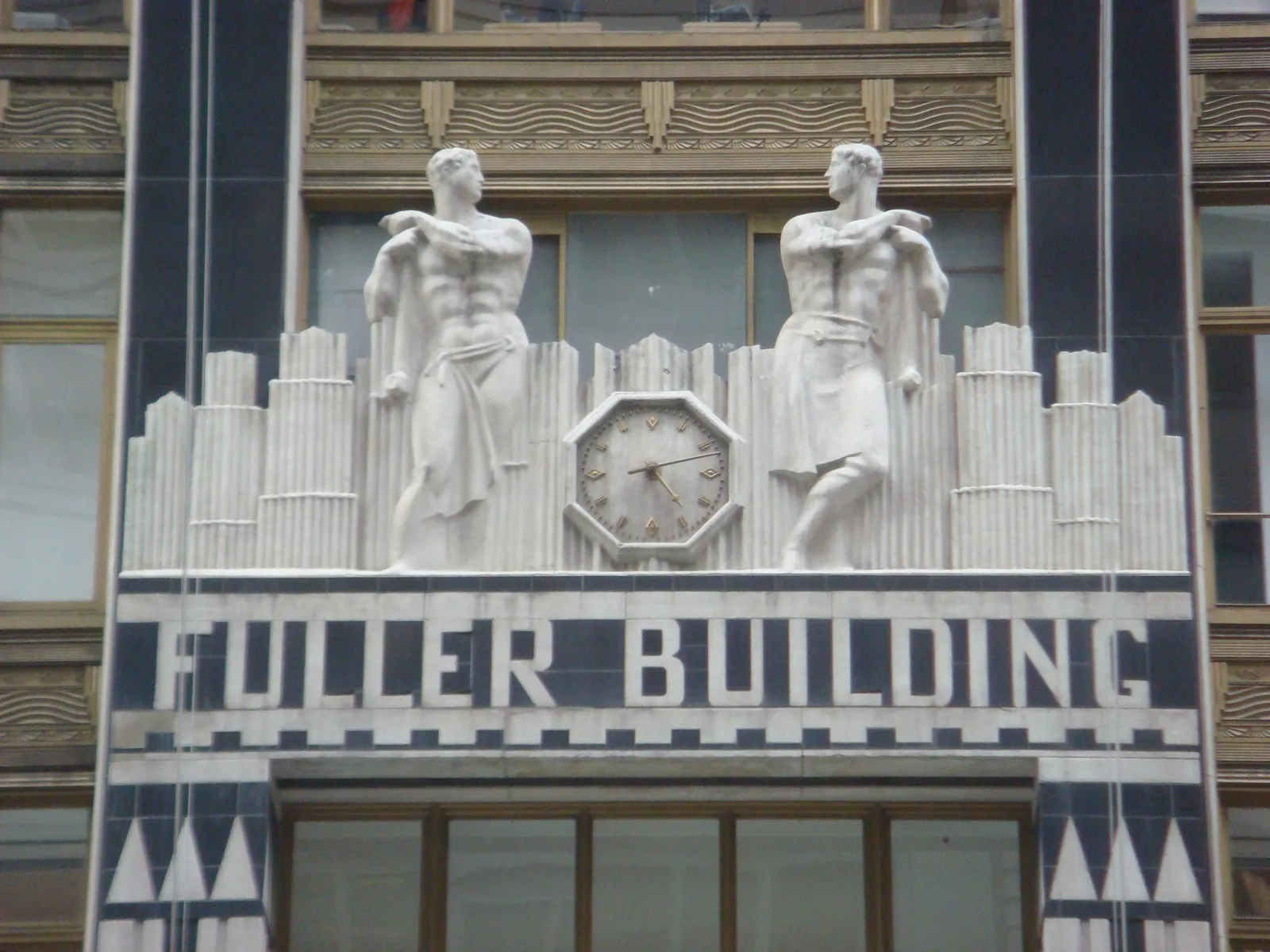 On the Art Deco facade of the Fuller Building, between two statues of athletic young men, there’s a clock that points at 12 minutes past 4.