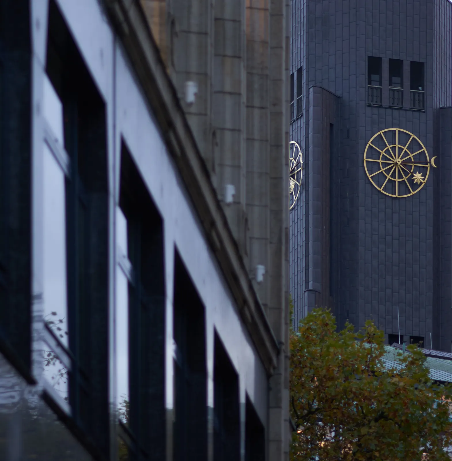 A huge golden clock on a black wall. There’s a moon attached to the end of the minute hand, and a sun to the end of the hour hand. It points at approximately 14 minutes past 4.