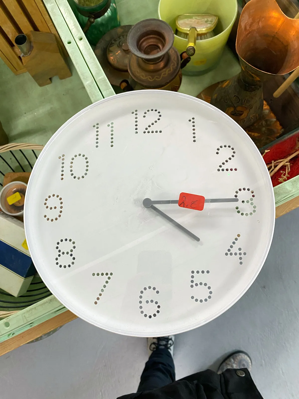 Crates with stuff for sale. On these crates there’s a white clock with the numbers made from little holes. It points at a quarter past 4.